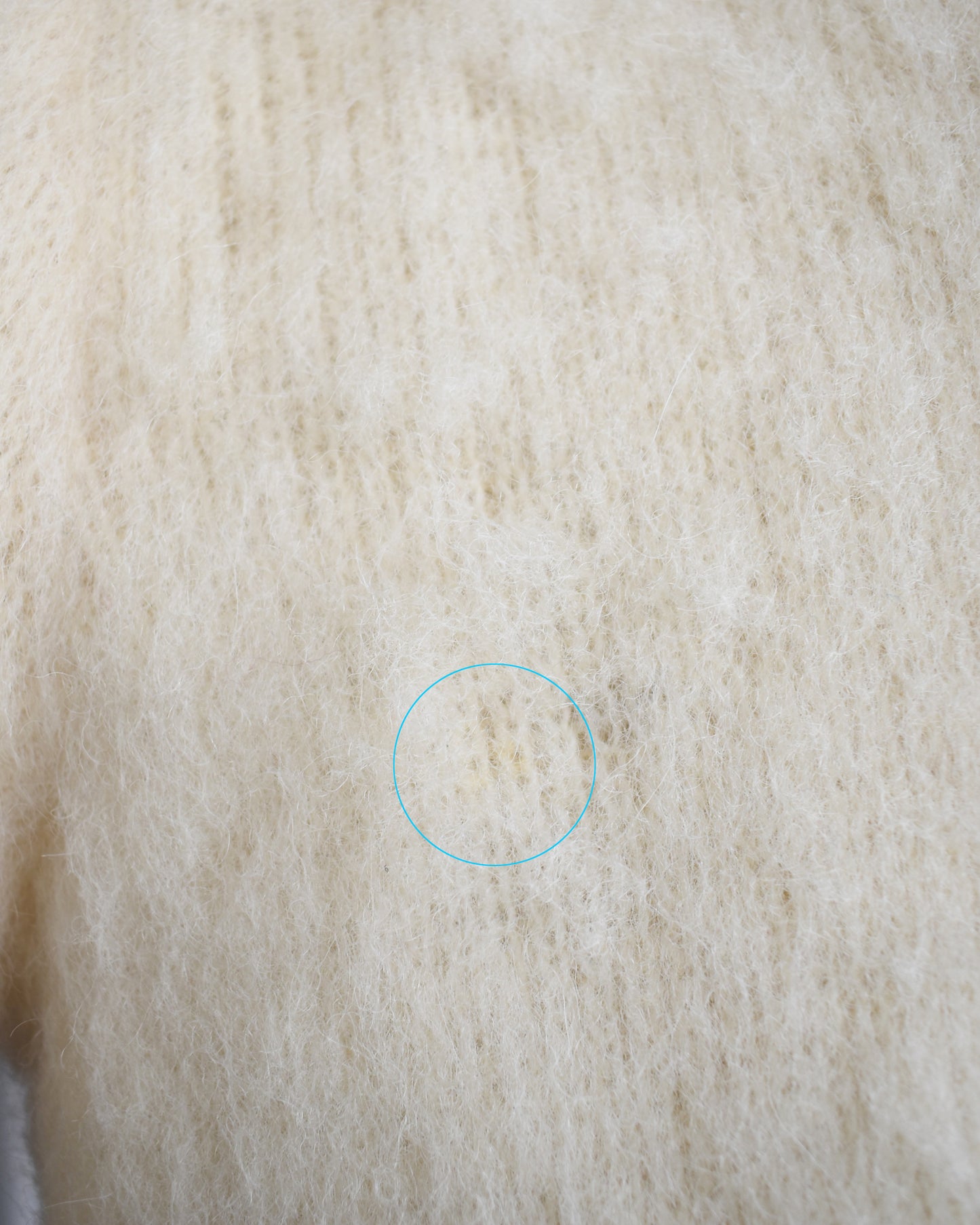 Close-up of beige fabric with a small stain highlighted by a blue circle.