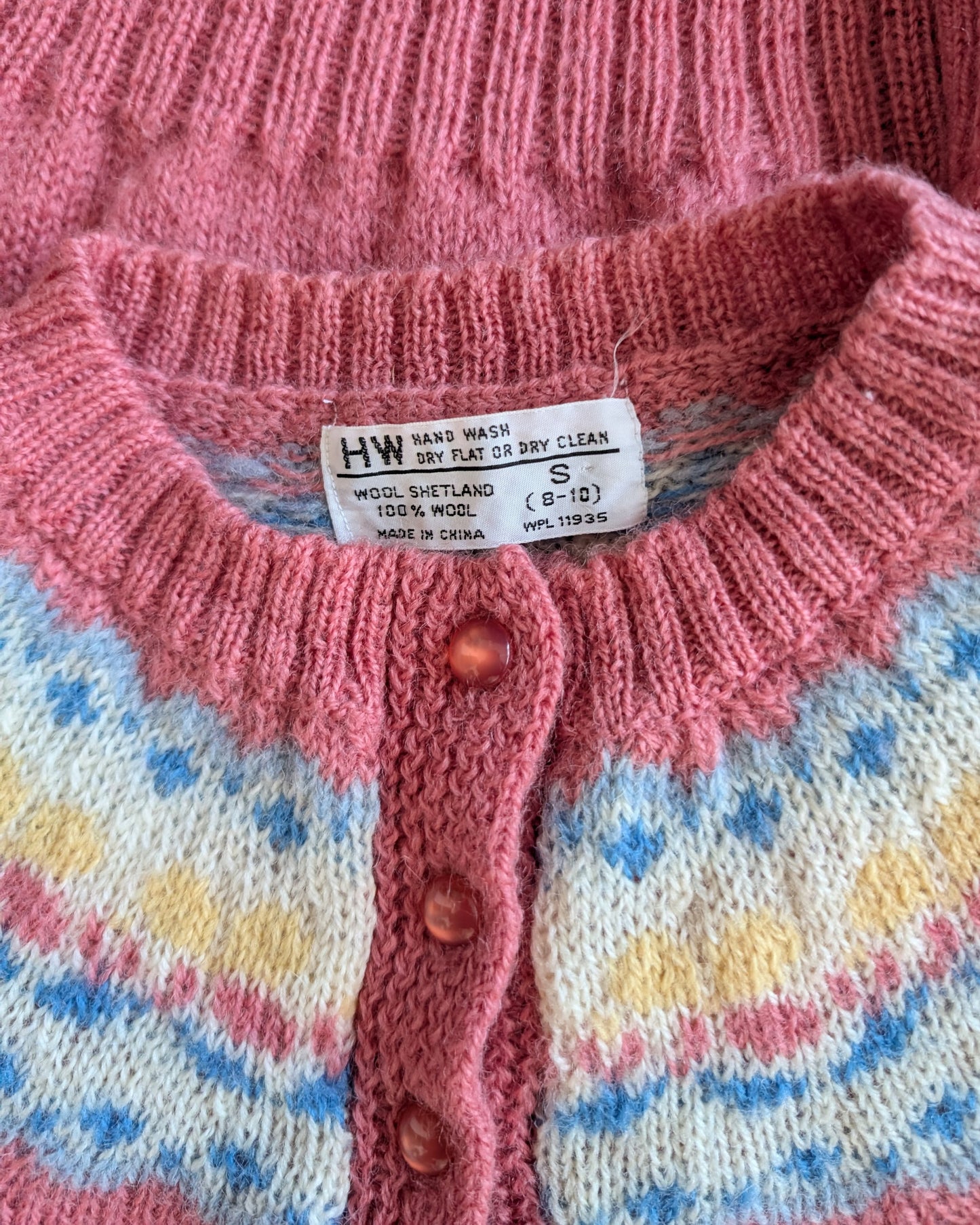 Close-up of a pink knitted cardigan with a label and patterned background