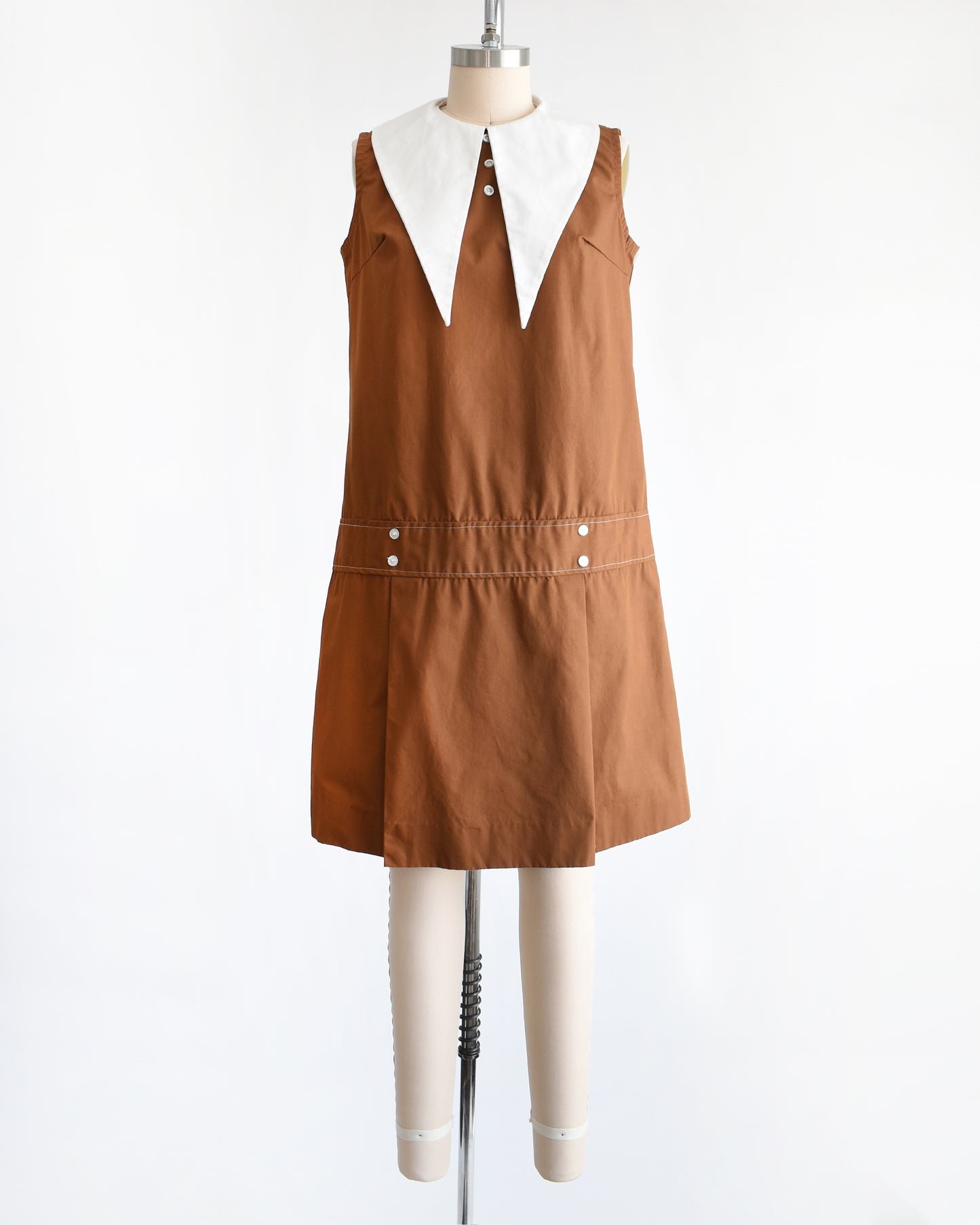 a vintage 1960s brown drop waist dress that has a large white dagger collar and decorative buttons on the front
