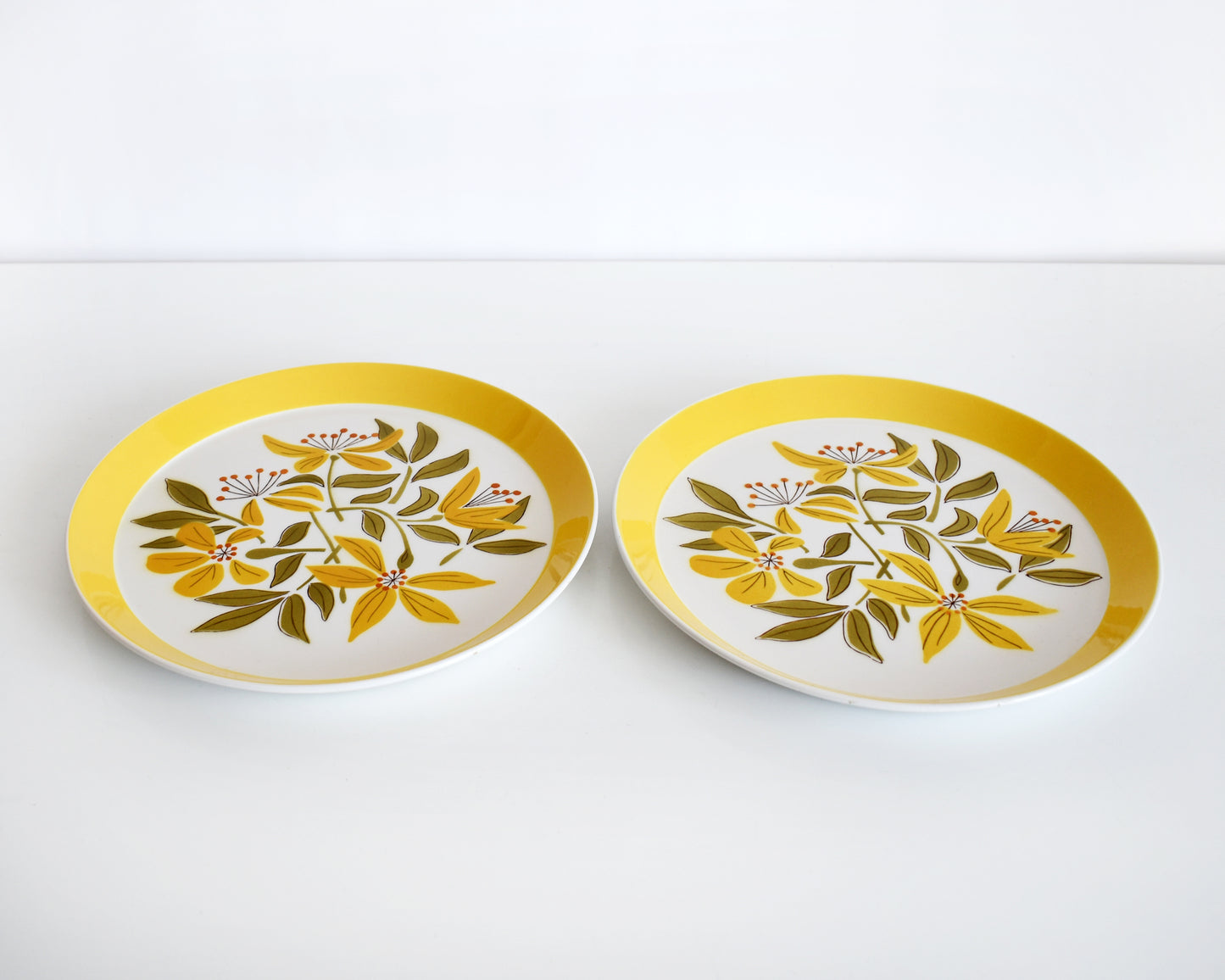 Two vintage 1970s plates from Mikasa Duplex line “Sunny Glow” D3504 pattern, designed by Ben Seibel. The plates have a wide yellow brim with a yellow, green, and orange floral motif at the center.