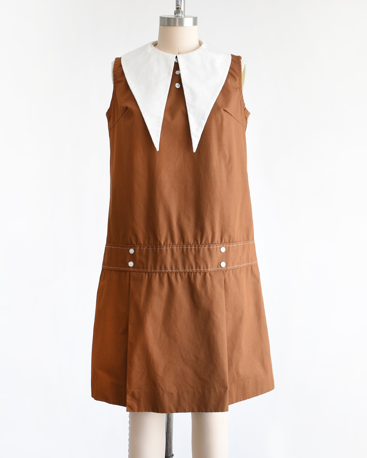 a vintage 1960s brown drop waist dress that has a large white dagger collar and decorative buttons on the front