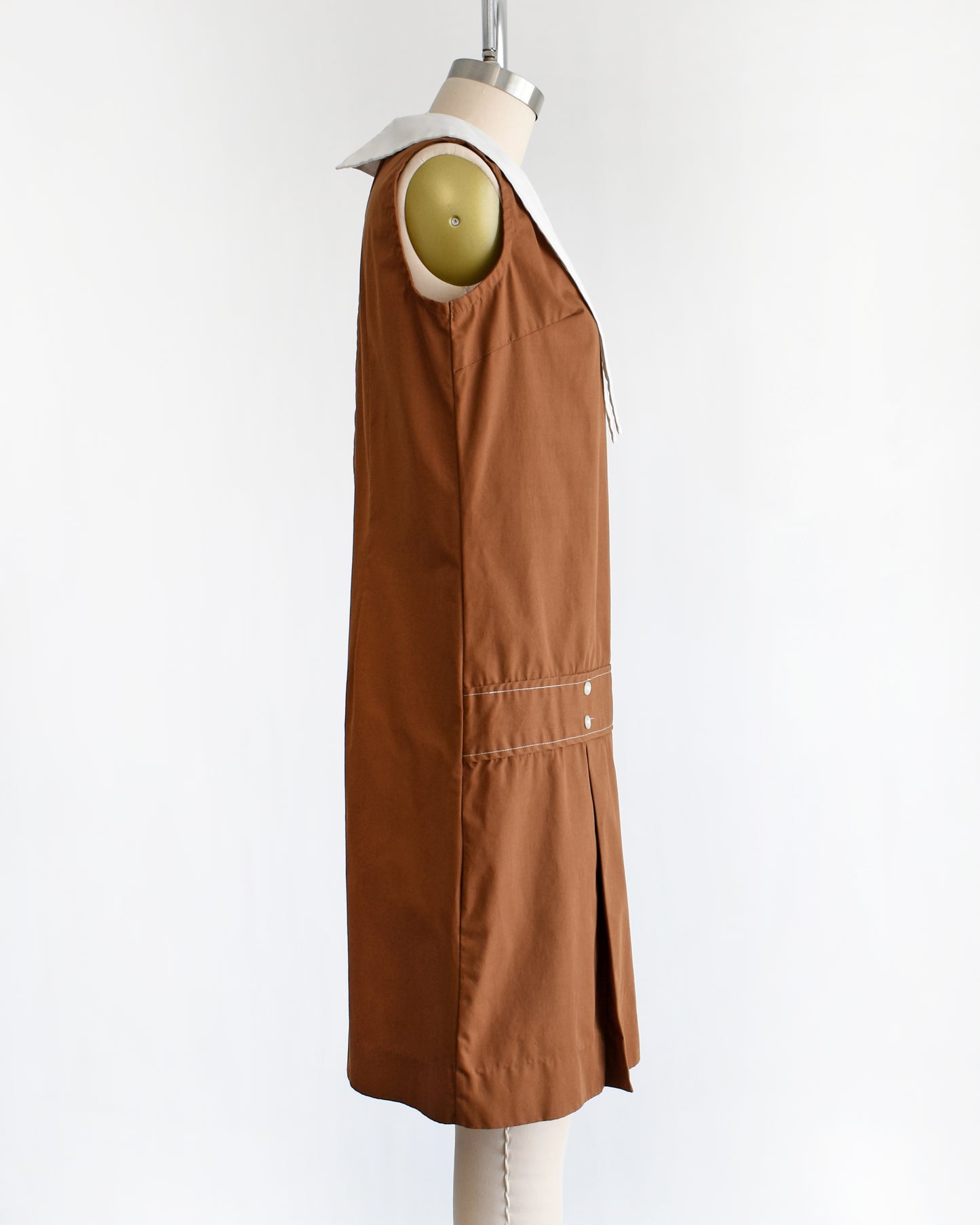 side view of a vintage 1960s brown drop waist dress that has a large white dagger collar and decorative buttons on the front