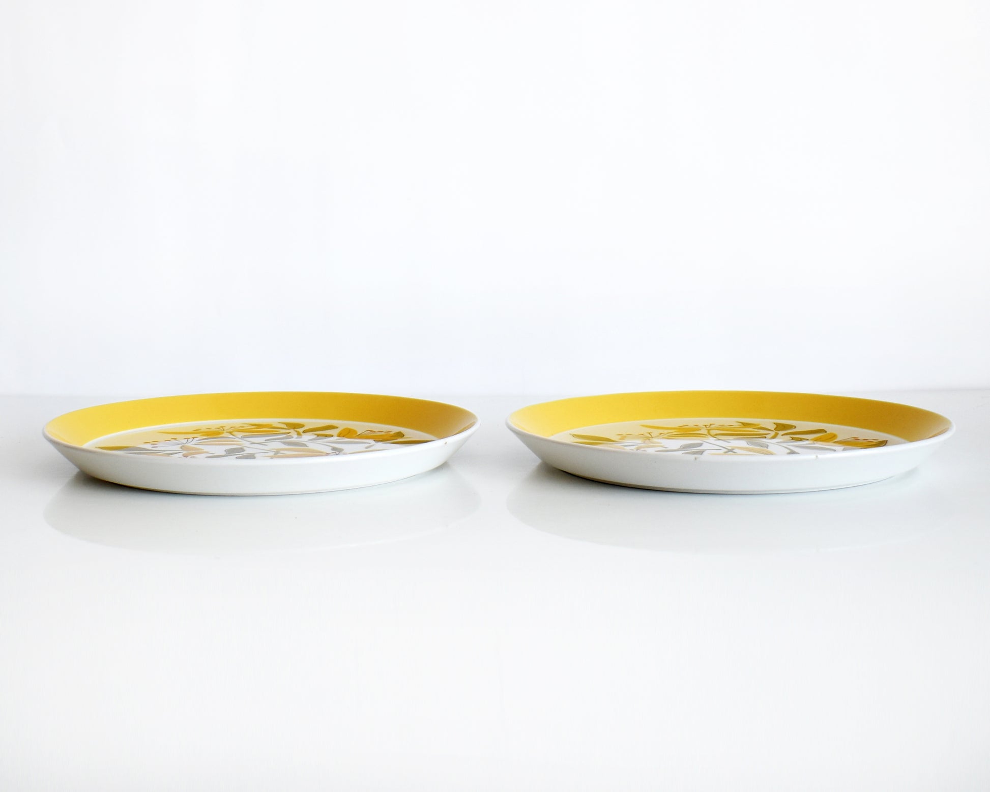 table view of two vintage 1970s plates from Mikasa Duplex line “Sunny Glow” D3504 pattern, designed by Ben Seibel. The plates have a wide yellow brim with a yellow, green, and orange floral motif at the center.