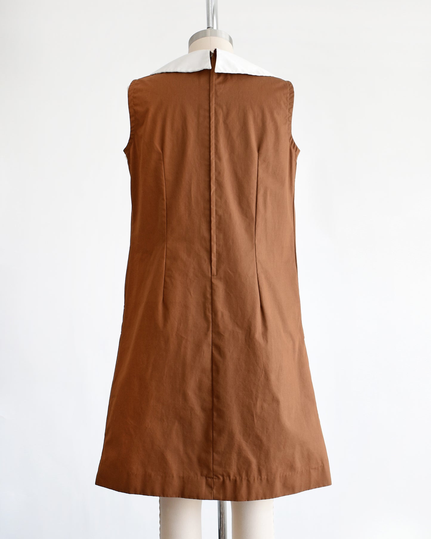 back view of a vintage 1960s brown drop waist dress that has a large white dagger collar and decorative buttons on the front