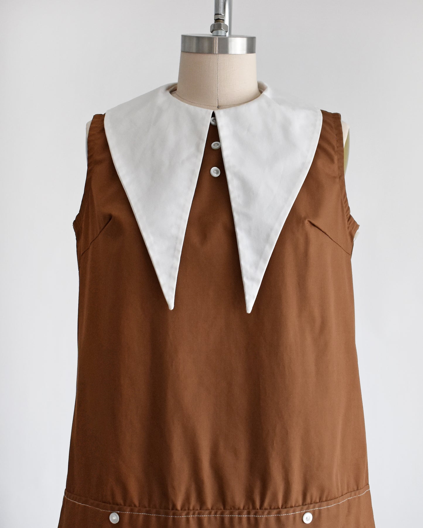 close up of a vintage 1960s brown drop waist dress that has a large white dagger collar and decorative buttons on the front