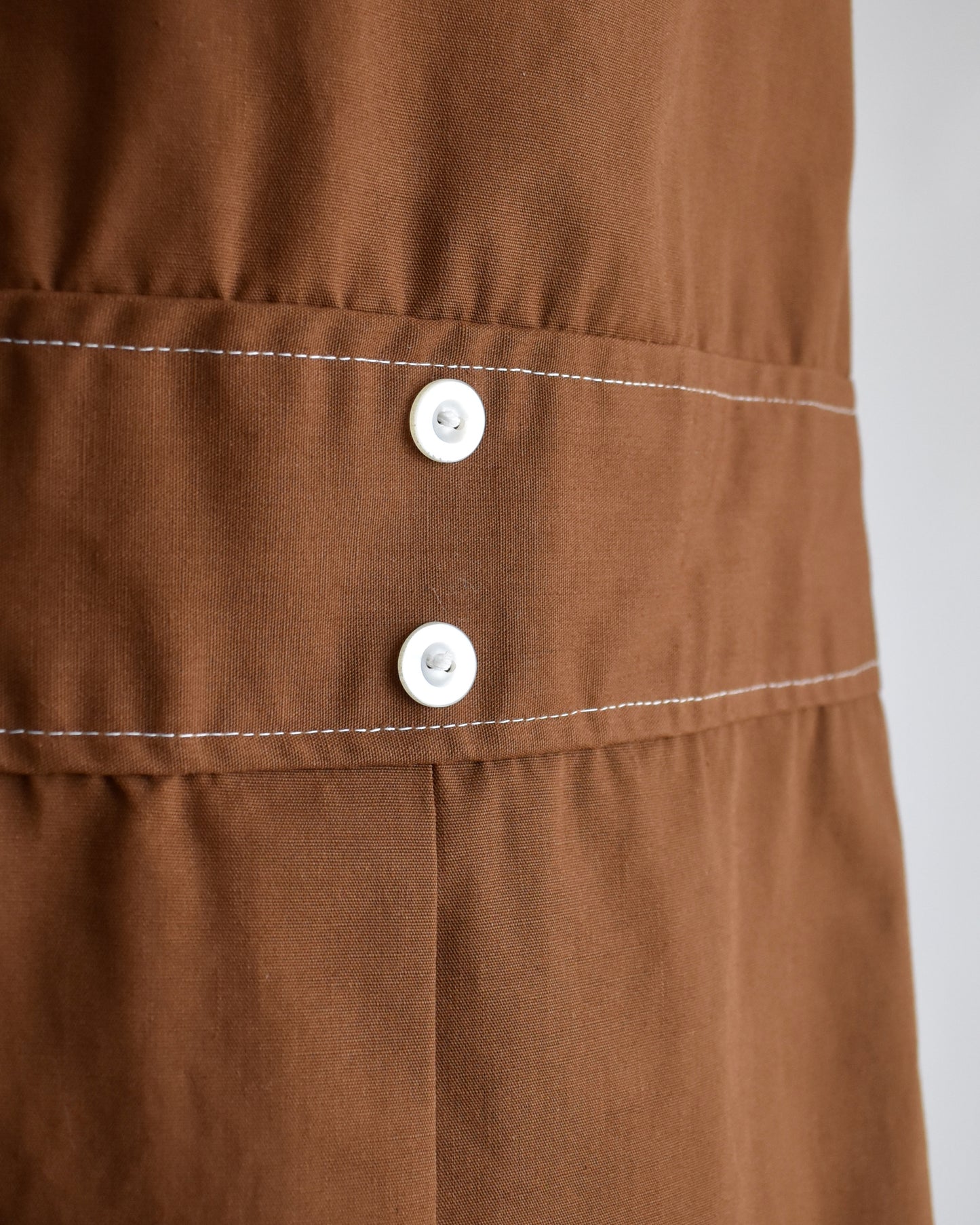 close up of the waist of a vintage 1960s brown drop waist dress that has a large white dagger collar and decorative buttons on the front