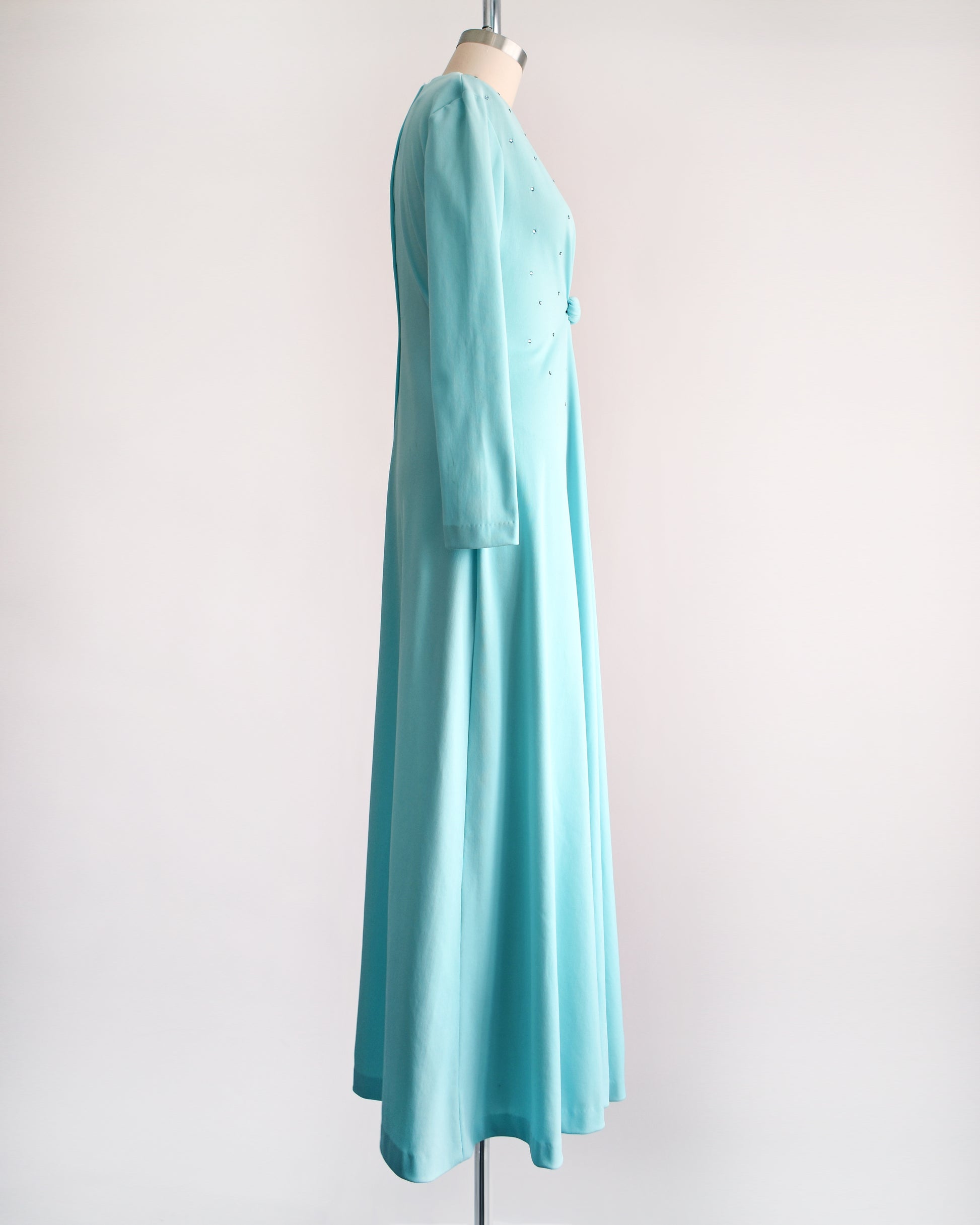 side view of a vintage 1970s light blue maxi dress that has rhinestones on the bodice, a plunging v-neckline, and long sleeves