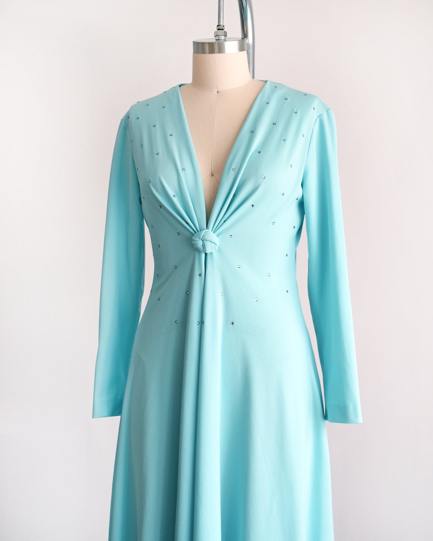 side front view of a vintage 1970s light blue maxi dress that has rhinestones on the bodice, a plunging v-neckline, and long sleeves