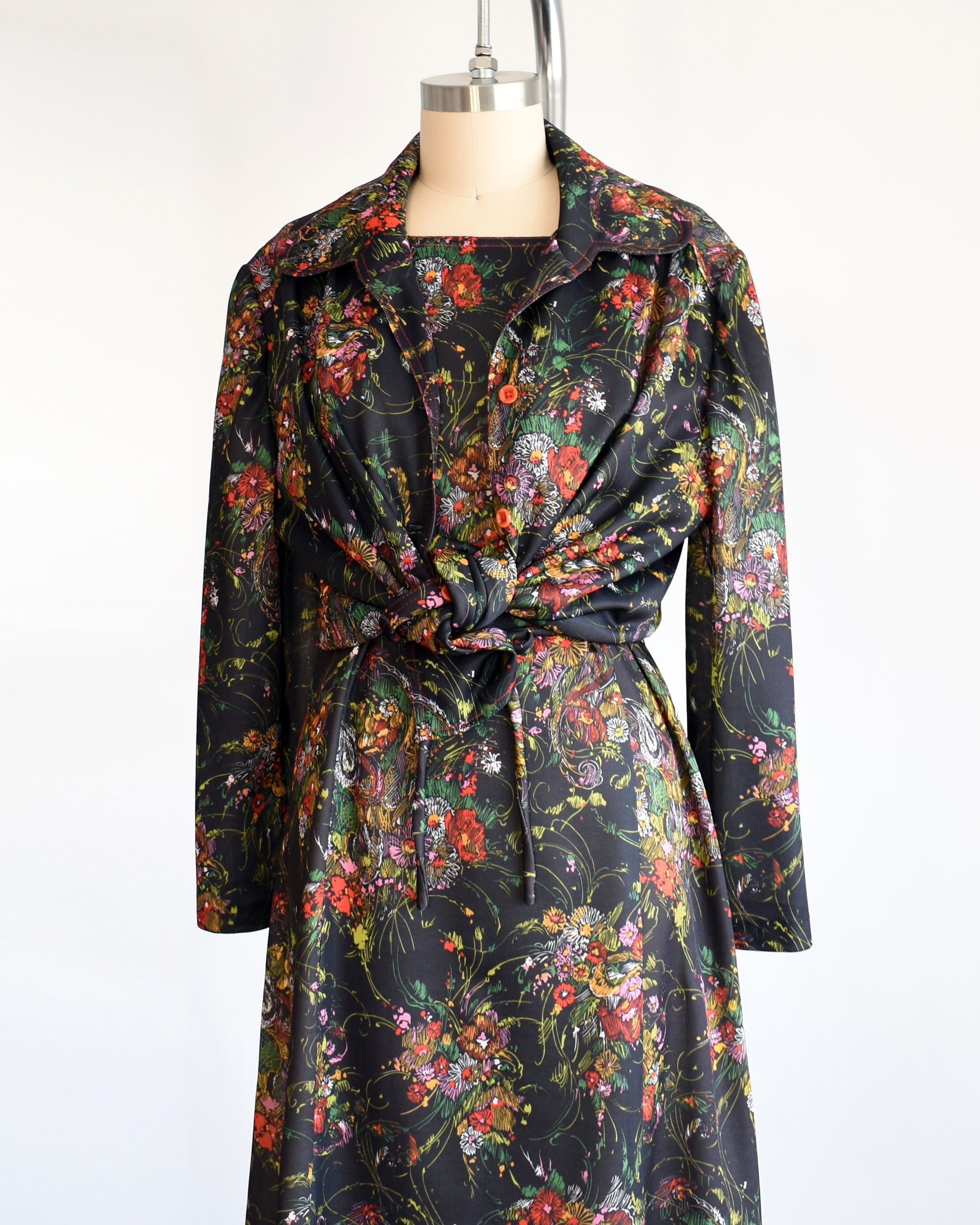side front view of a vintage 1970s black floral dress set that comes with a dress, a matching top, and belt. the top is tied in this photo