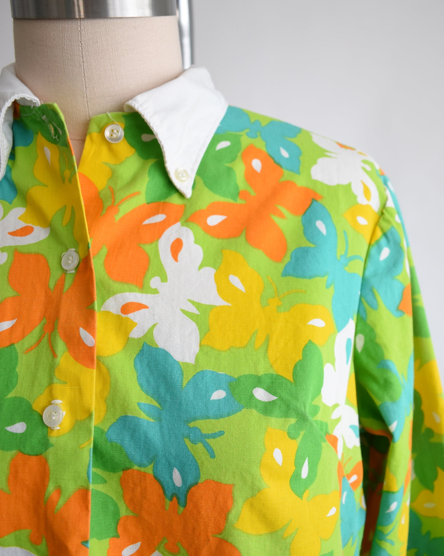close up of the button down collar on a vintage 1960s green long sleeve romper with multicolored butterfly print all over