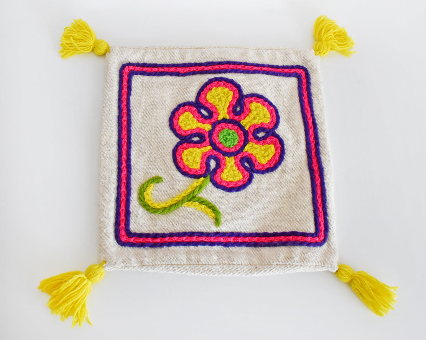 A vintage crewel embroidered floral pillow cover with yellow tassels on a table.