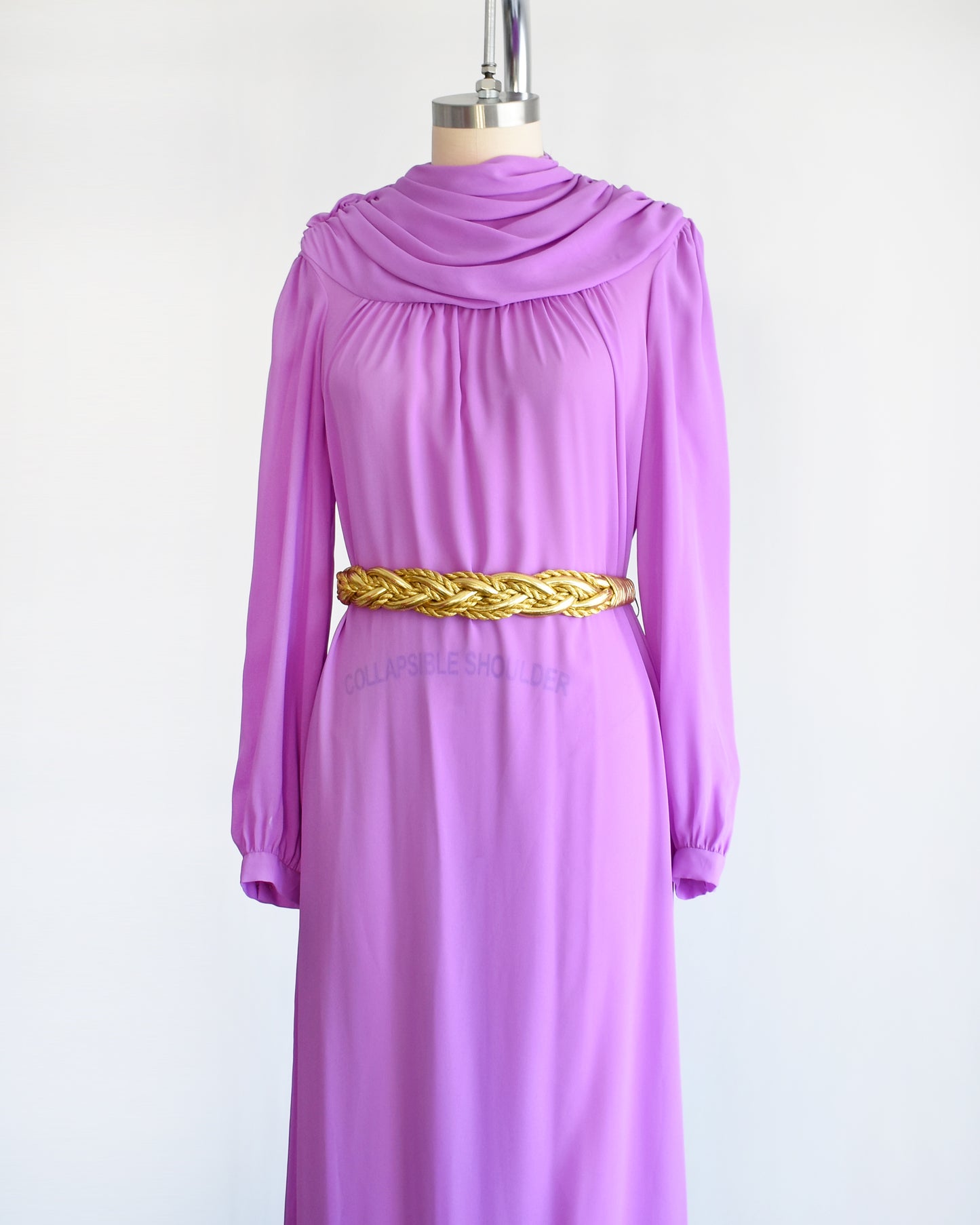 Side front view of a vintage 1970s purple semi sheer maxi dress by Joy Stevens California that has a draped neckline and long sleeves with gold belt which isn't included