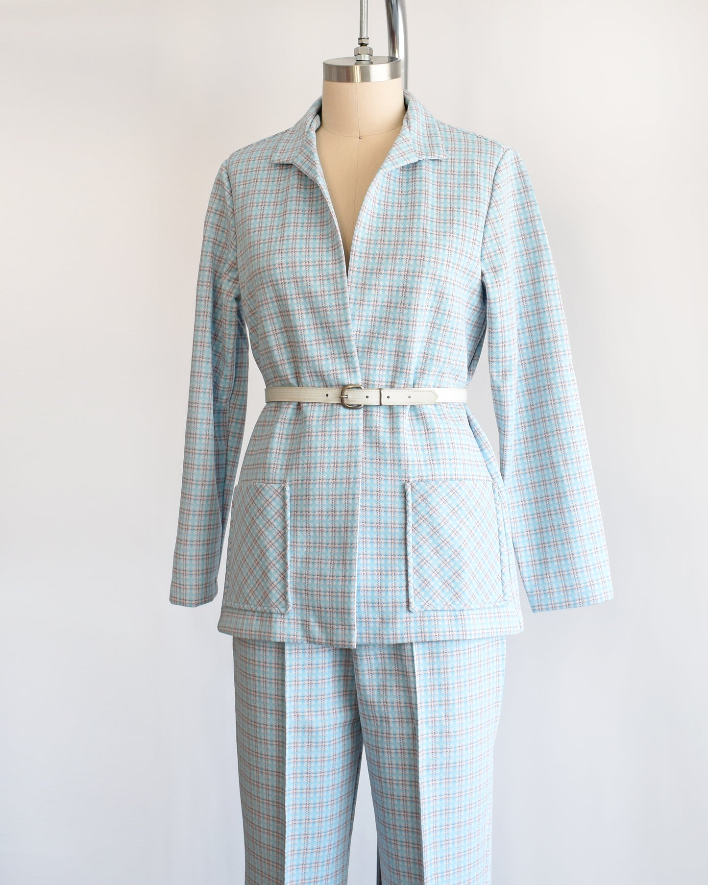 Side front view of a  vintage 1970s blue, white, and orange plaid pantsuit. This set includes a blazer and matching wide leg pants. The set is modeled with a white belt which isn't included.