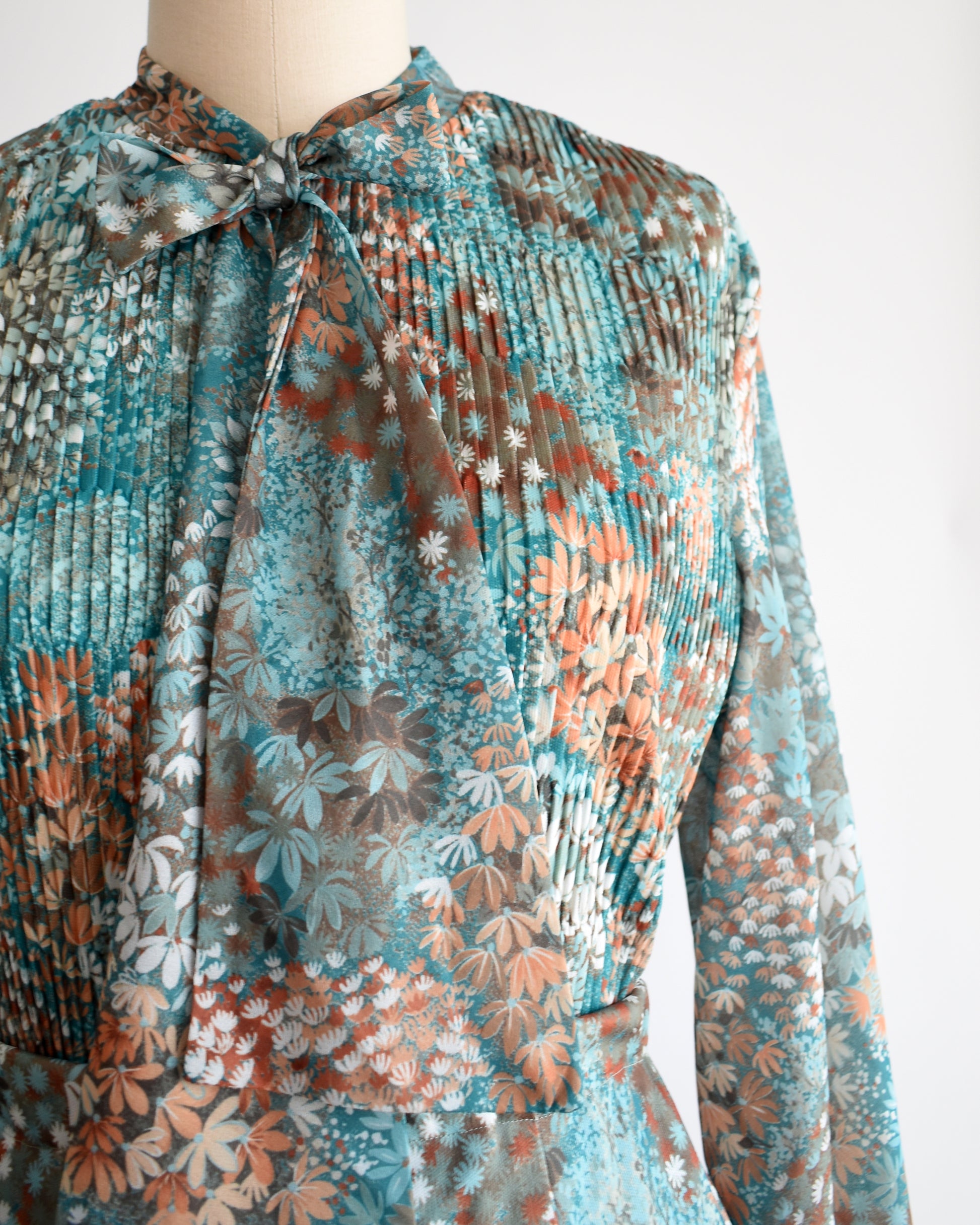 Close up of the blouse which shows the ascot bow, micro-pleats, and floral print