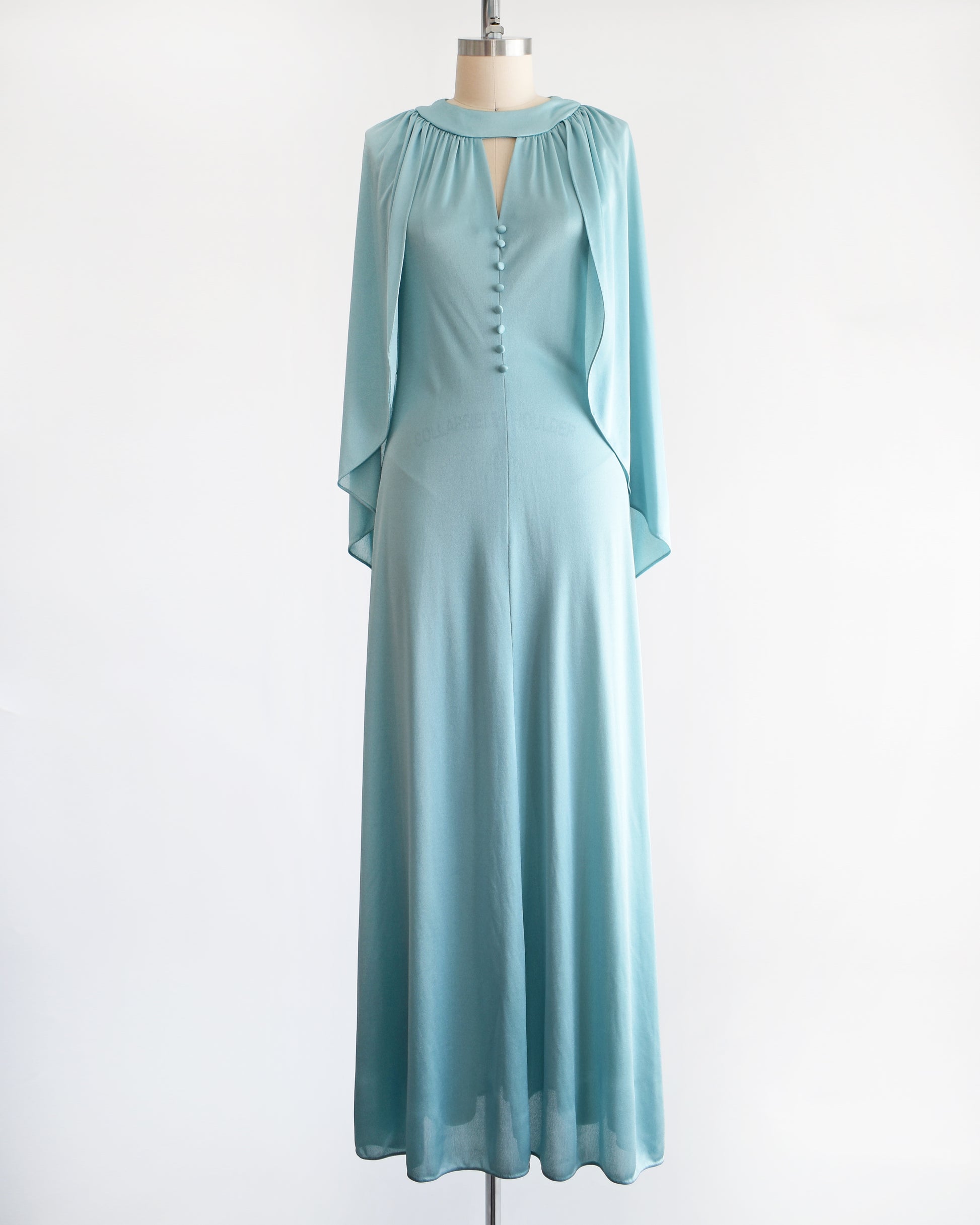 A vintage 1970s seafoam blue caped maxi dress that has a triangle keyhole cutout and decorative buttons down the front