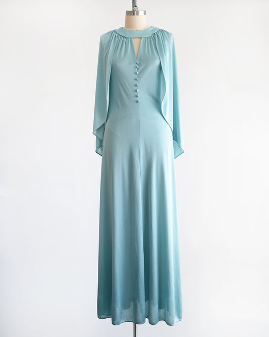A vintage 1970s seafoam blue caped maxi dress that has a triangle keyhole cutout and decorative buttons down the front