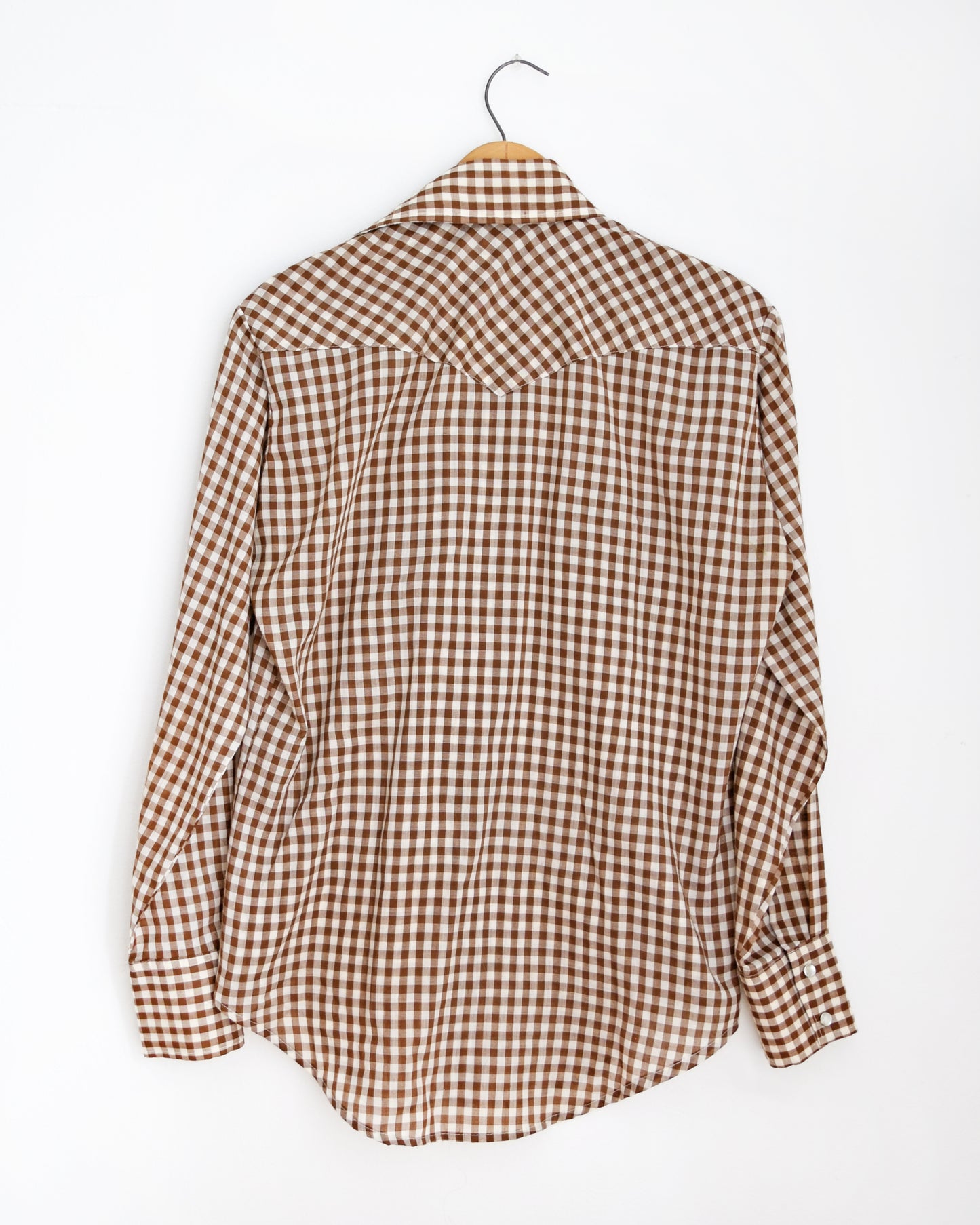 back view of a vintage 1970s brown and white gingham pearl snap shirt on a hanger