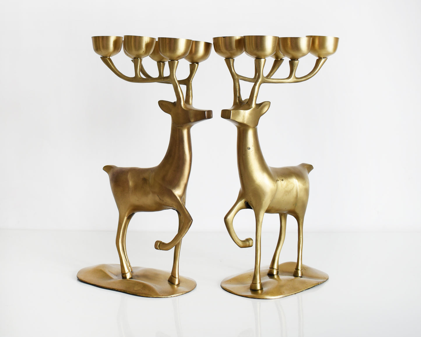 A pair of large vintage brass deer candelabras that have six tea light candle holders on top of their antlers.