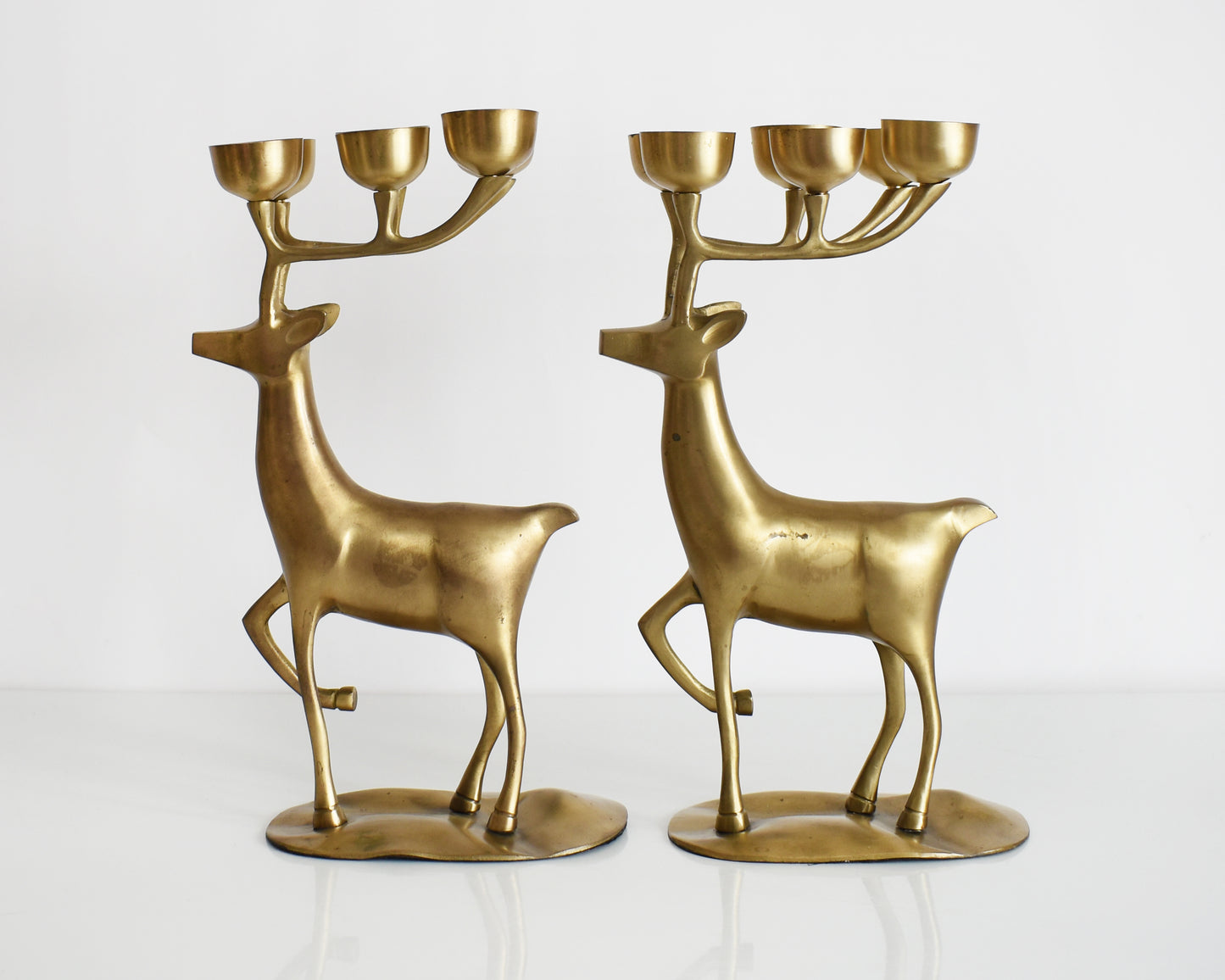 A pair of large vintage brass deer candelabras that have six tea light candle holders on top of their antlers