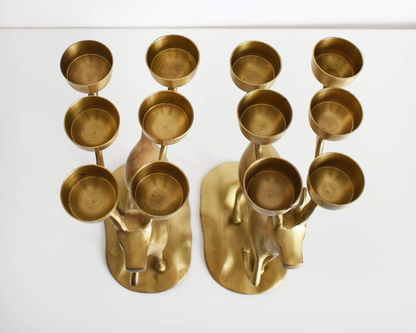 Overhead shot of a pair of large vintage brass deer candelabras that have six tea light candle holders on top of their antlers