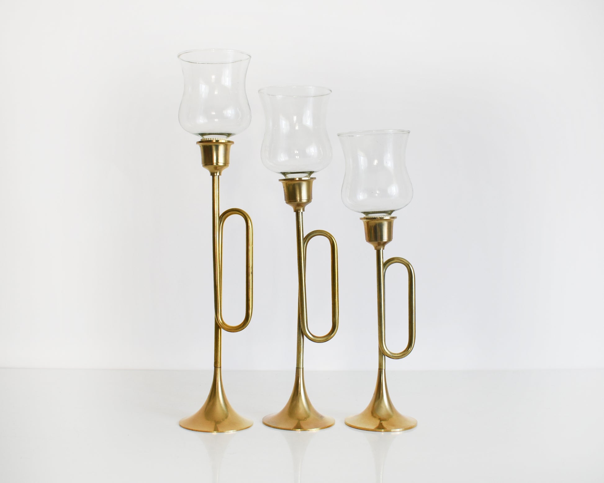 Three vintage brass bugle/horn candlesticks that has clear class votives on top.