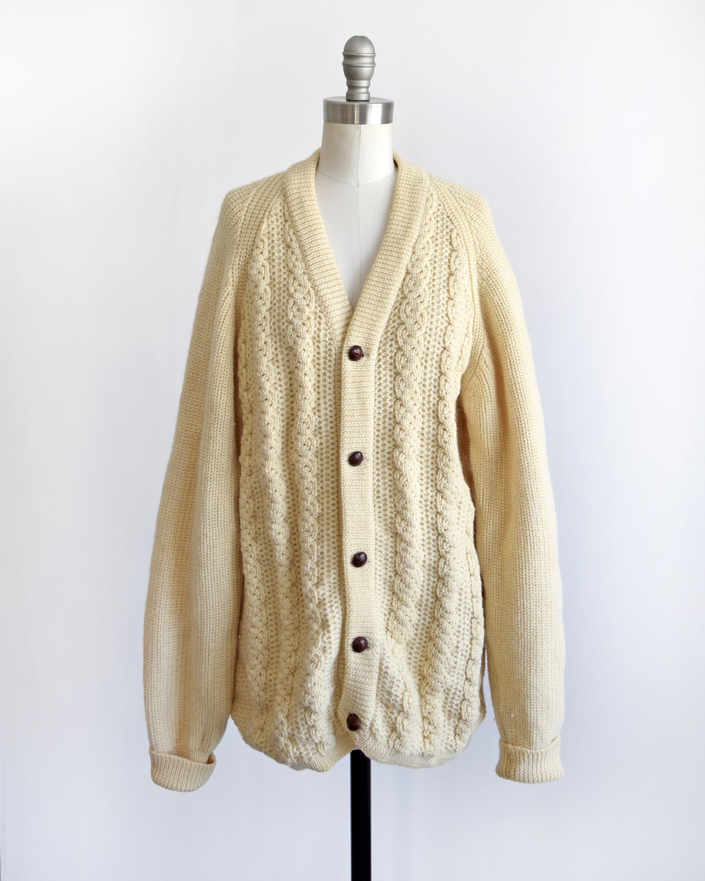 A vintage cream cable knit cardigan with dark buttons down the front. The cardigan is modeled on a dress form.