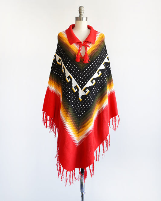 A vintage 1970s chevron striped fringe poncho that has a folded over red collar with and two tassels that can be tied into a bow.