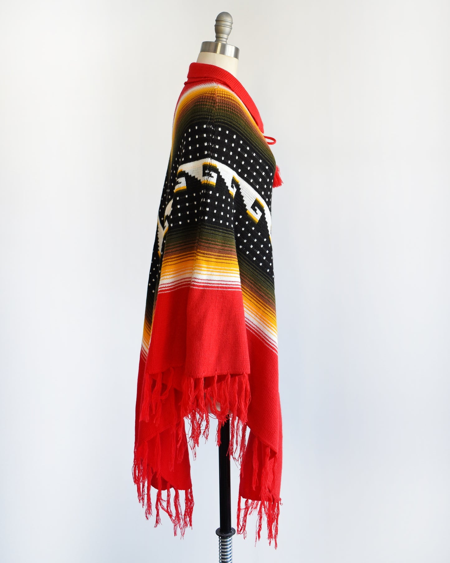 Side view of a vintage 1970s chevron striped fringe poncho that has a folded over red collar with and two tassels that can be tied into a bow.