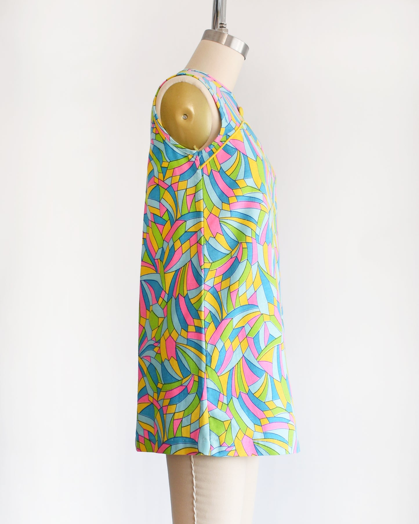 side view of a vintage 1960s micro mini dress with a dark and light blue, pink, green, yellow kaleidoscope print