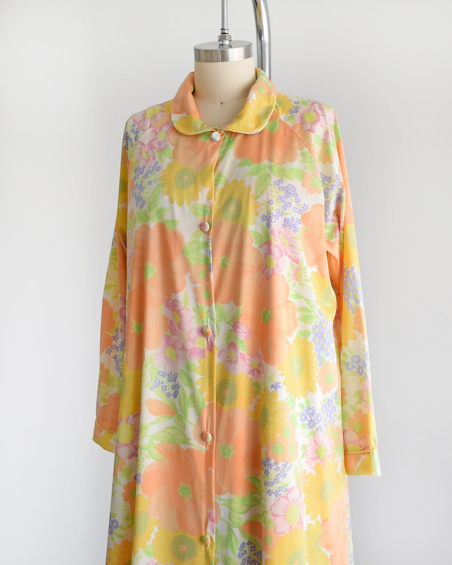 Side front view of a vintage 1970s floral peignoir set by Lorraine. This set includes a nightgown and matching button up long sleeve robe that is white and has an orange, yellow, pink, purple, and green floral print. 