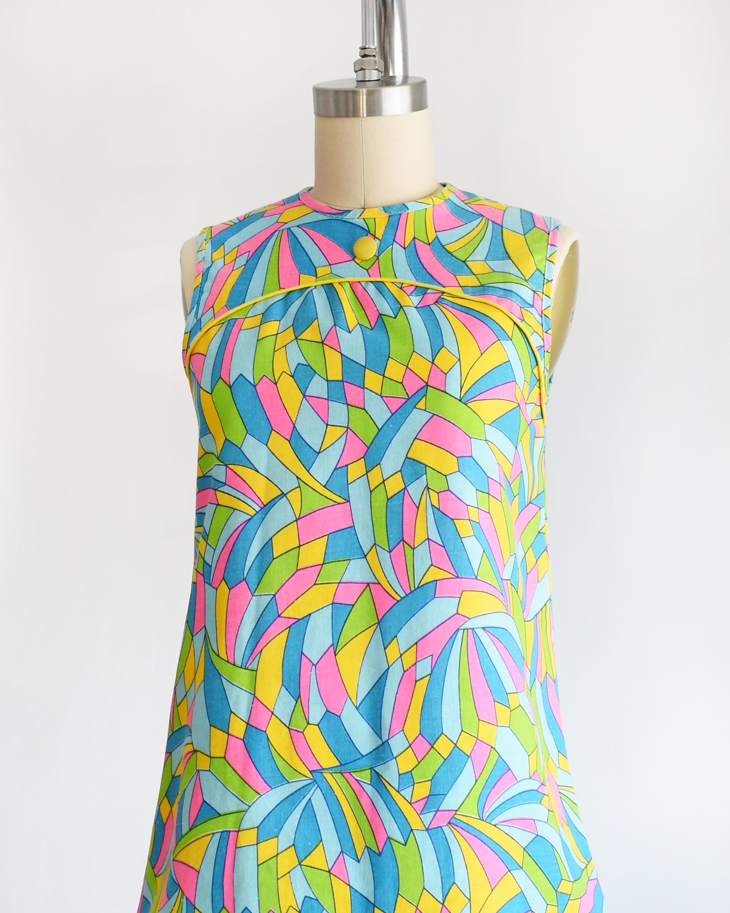 side front view of a vintage 1960s micro mini dress with a dark and light blue, pink, green, yellow kaleidoscope print