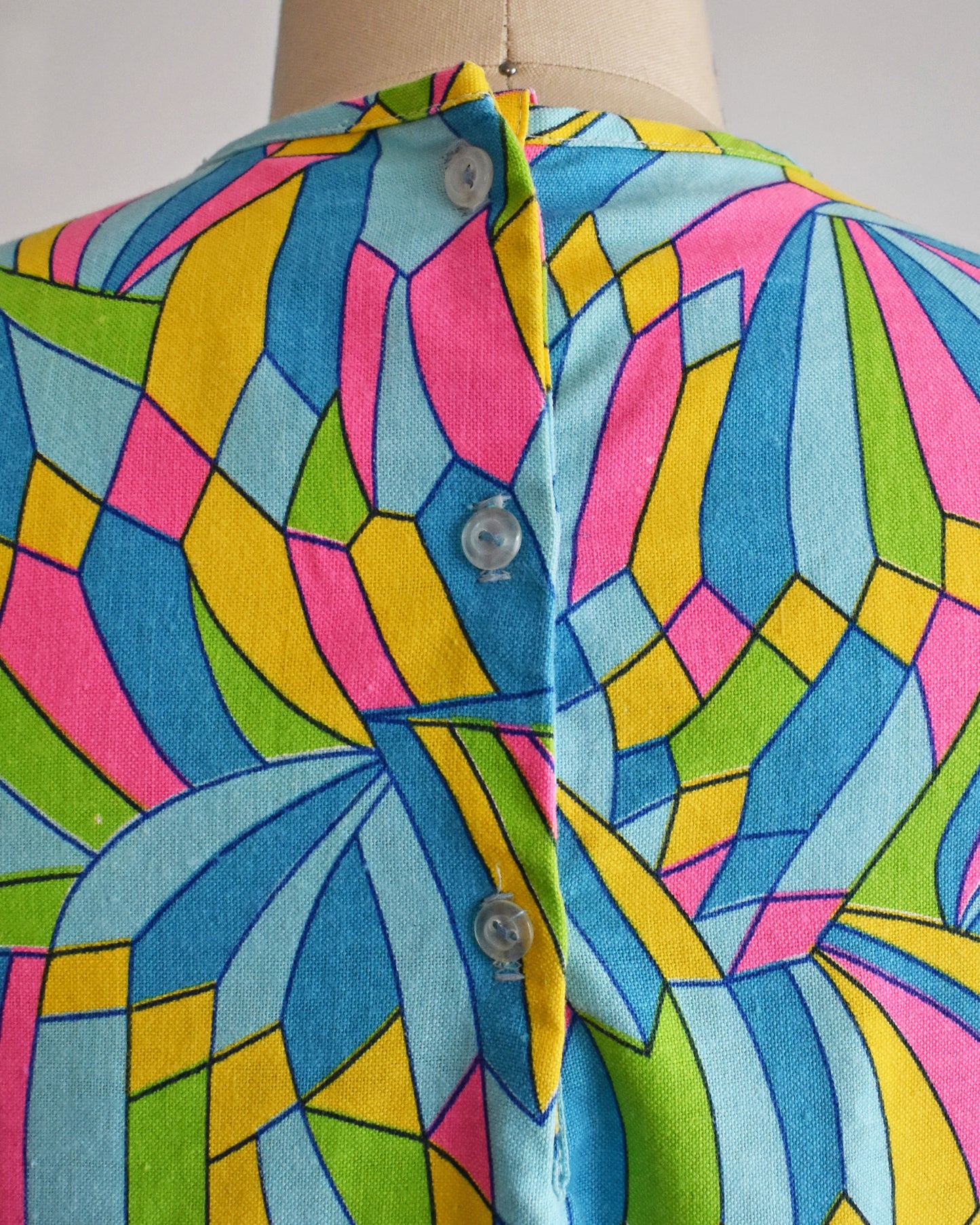 close up of the three back buttons on a vintage 1960s micro mini dress with a dark and light blue, pink, green, yellow kaleidoscope print