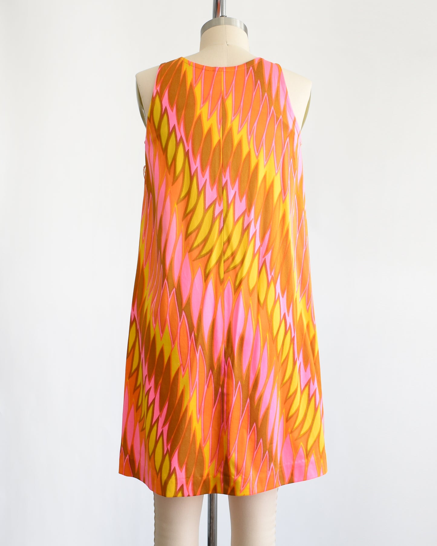 back view of a vintage 1960s mini dress that has a psychedelic print in orange, pink, yellow, and brown