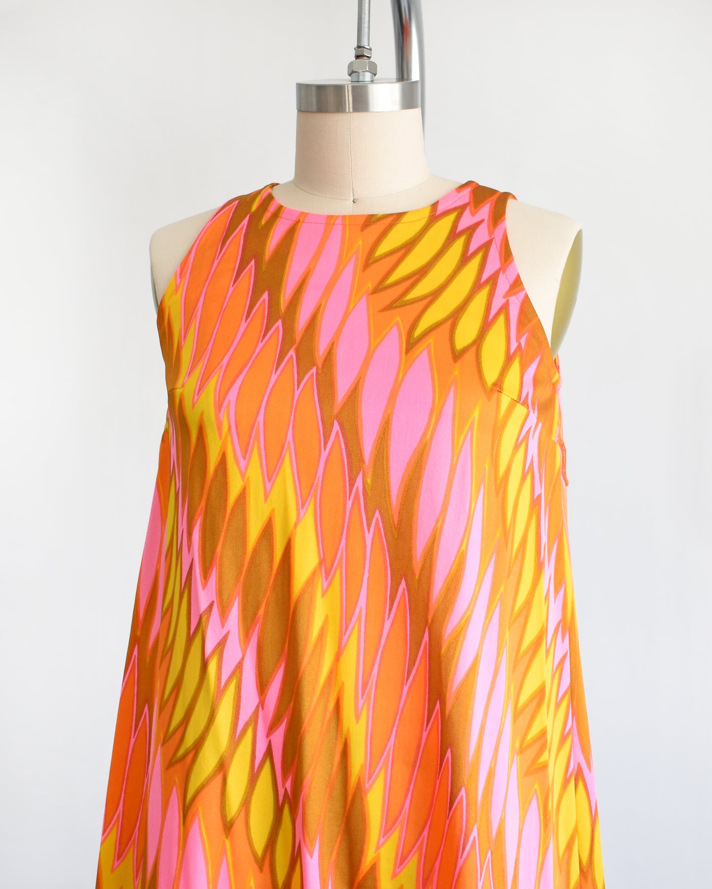 side front view of a vintage 1960s mini dress that has a psychedelic print in orange, pink, yellow, and brown