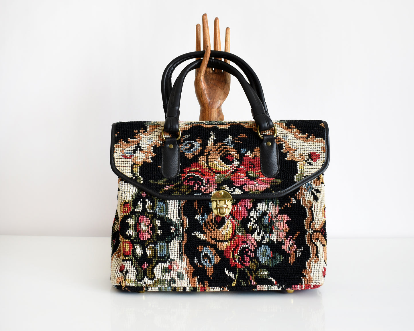a 1960s floral needlepoint tapestry purse with a wooden hand behind it