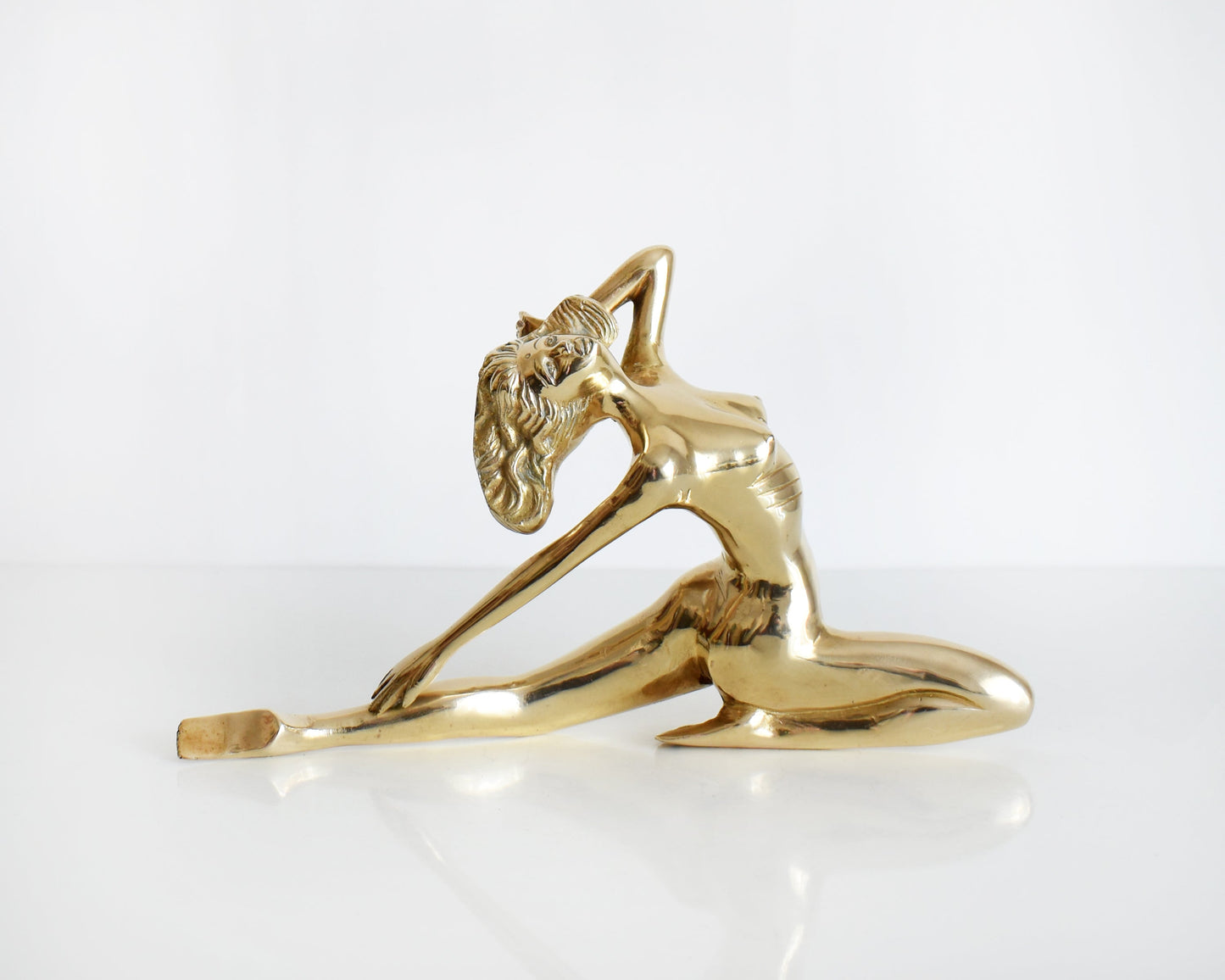A vintage 1970s nude brass woman that is posed with one arm bent, another stretched behind her, and one leg also stretched out and the other leg is bent at the knee.  