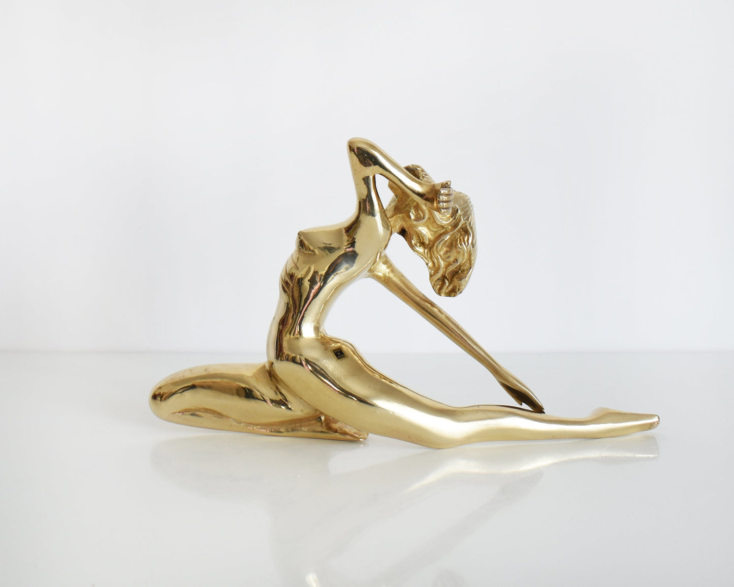 back view of a vintage 1970s nude brass woman that is posed with one arm bent, another stretched behind her, and one leg also stretched out and the other leg is bent at the knee.