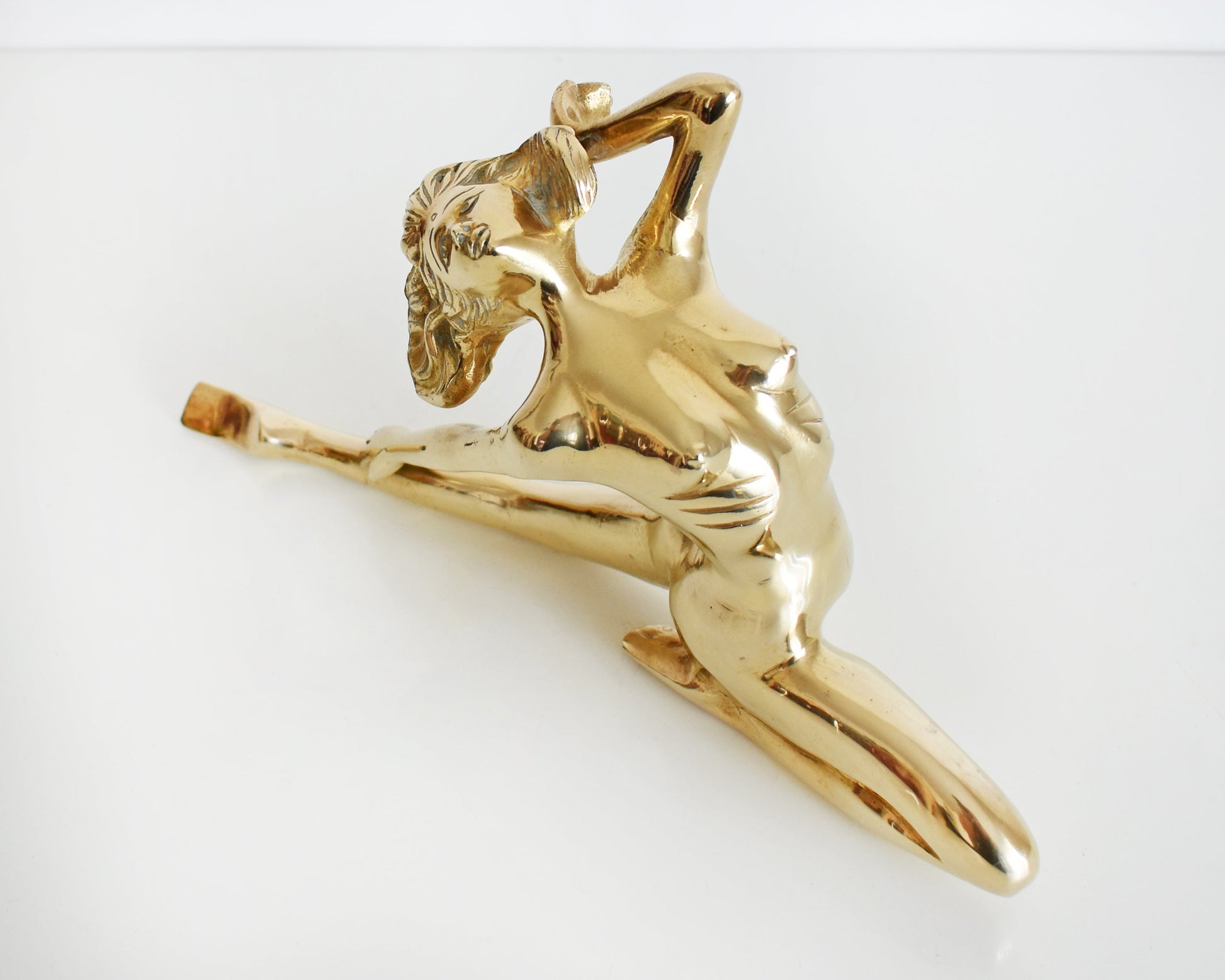 overhead front view of a vintage 1970s nude brass woman that is posed with one arm bent, another stretched behind her, and one leg also stretched out and the other leg is bent at the knee.  
