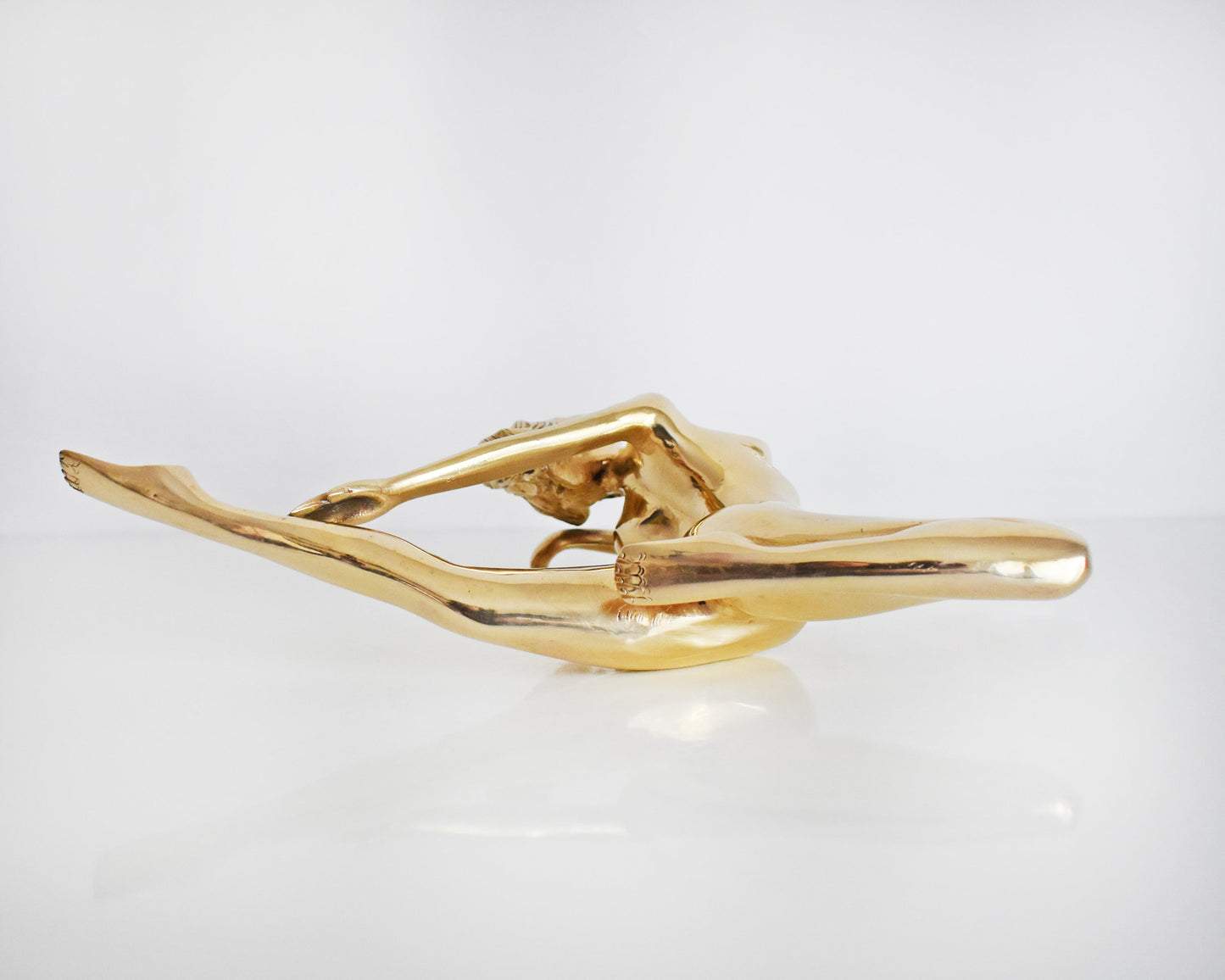 underside view of a vintage 1970s nude brass woman that is posed with one arm bent, another stretched behind her, and one leg also stretched out and the other leg is bent at the knee.