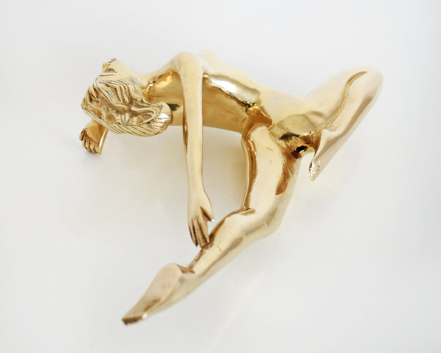 overhead shot of the back of a vintage 1970s nude brass woman that is posed with one arm bent, another stretched behind her, and one leg also stretched out and the other leg is bent at the knee.