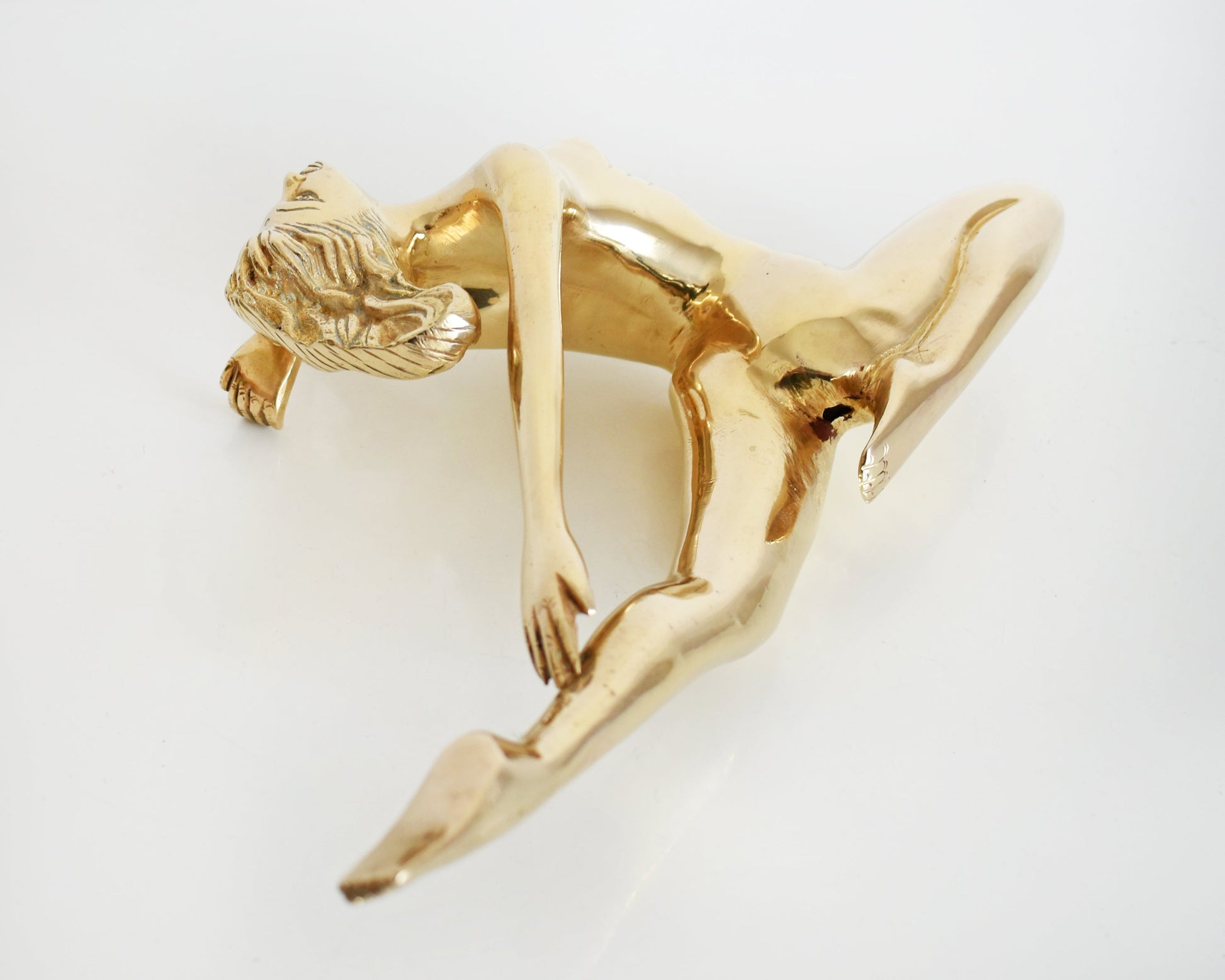 overhead shot of the back of a vintage 1970s nude brass woman that is posed with one arm bent, another stretched behind her, and one leg also stretched out and the other leg is bent at the knee.  