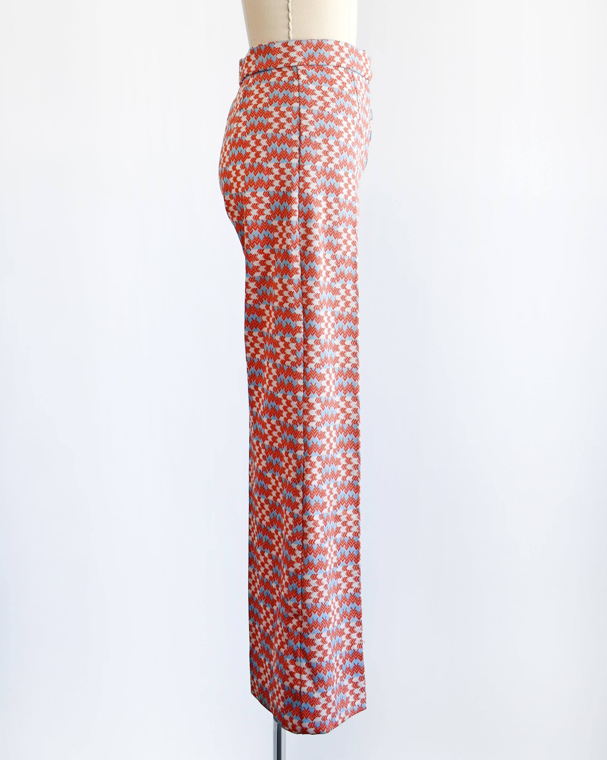 side view of a vintage 1970s wide leg pants feature a vibrant print with dark orange, white, and light blue arrows pointing in various directions down the legs.