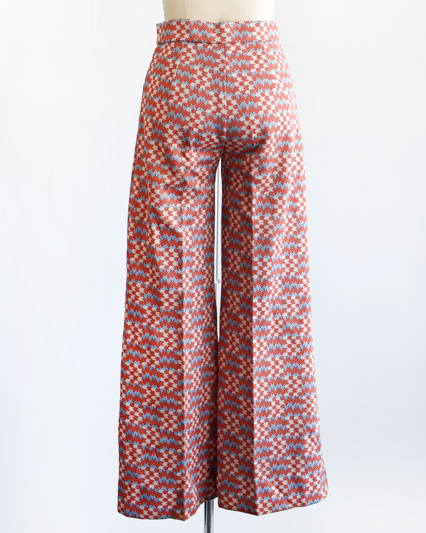 back view of  a vintage 1970s wide leg pants feature a vibrant print with dark orange, white, and light blue arrows pointing in various directions down the legs.