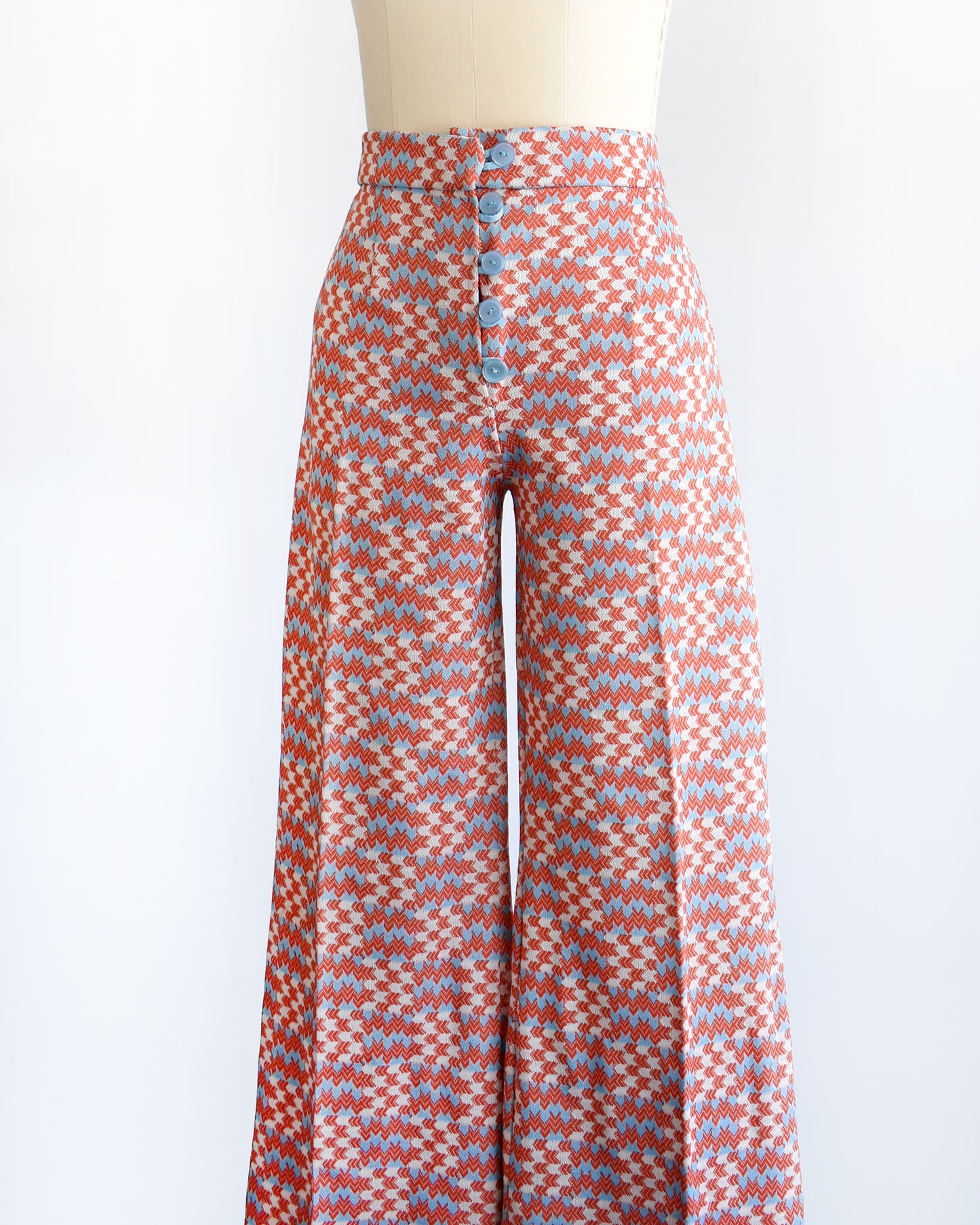 side front view of a vintage 1970s wide leg pants feature a vibrant print with dark orange, white, and light blue arrows pointing in various directions down the legs. There are 5 buttons on the front of the pants