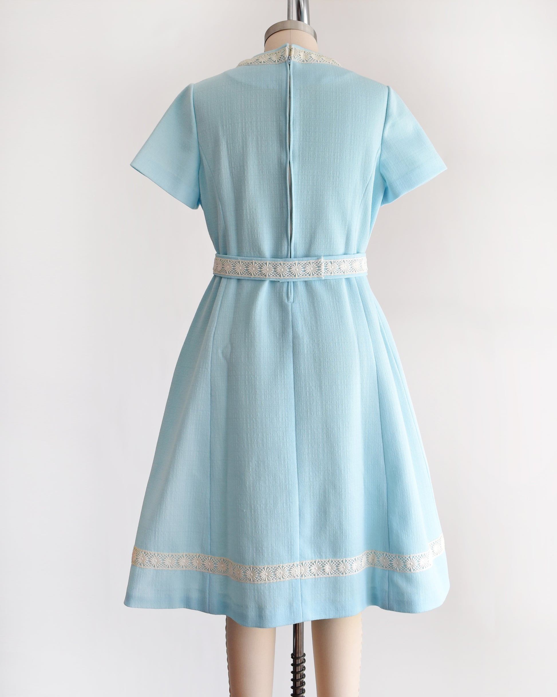 back view of a late 1960s early 1970s vintage mod dress that is light blue and has cream floral lace trim around the collar, belt, and hem