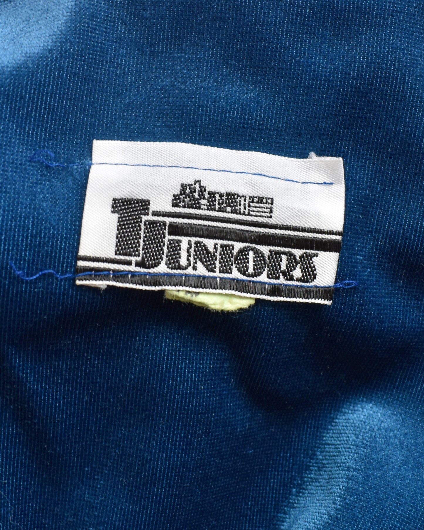 Close-up of a 'T Juniors' label on a blue fabric background
