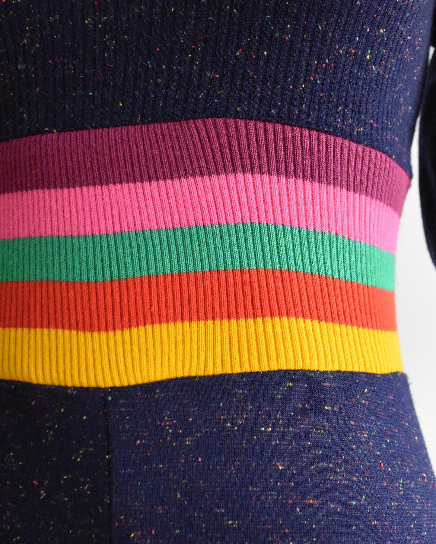 close up of the waist of a vintage 1970s purple blue dress with a colorful striped waistband on a mannequin against a white background