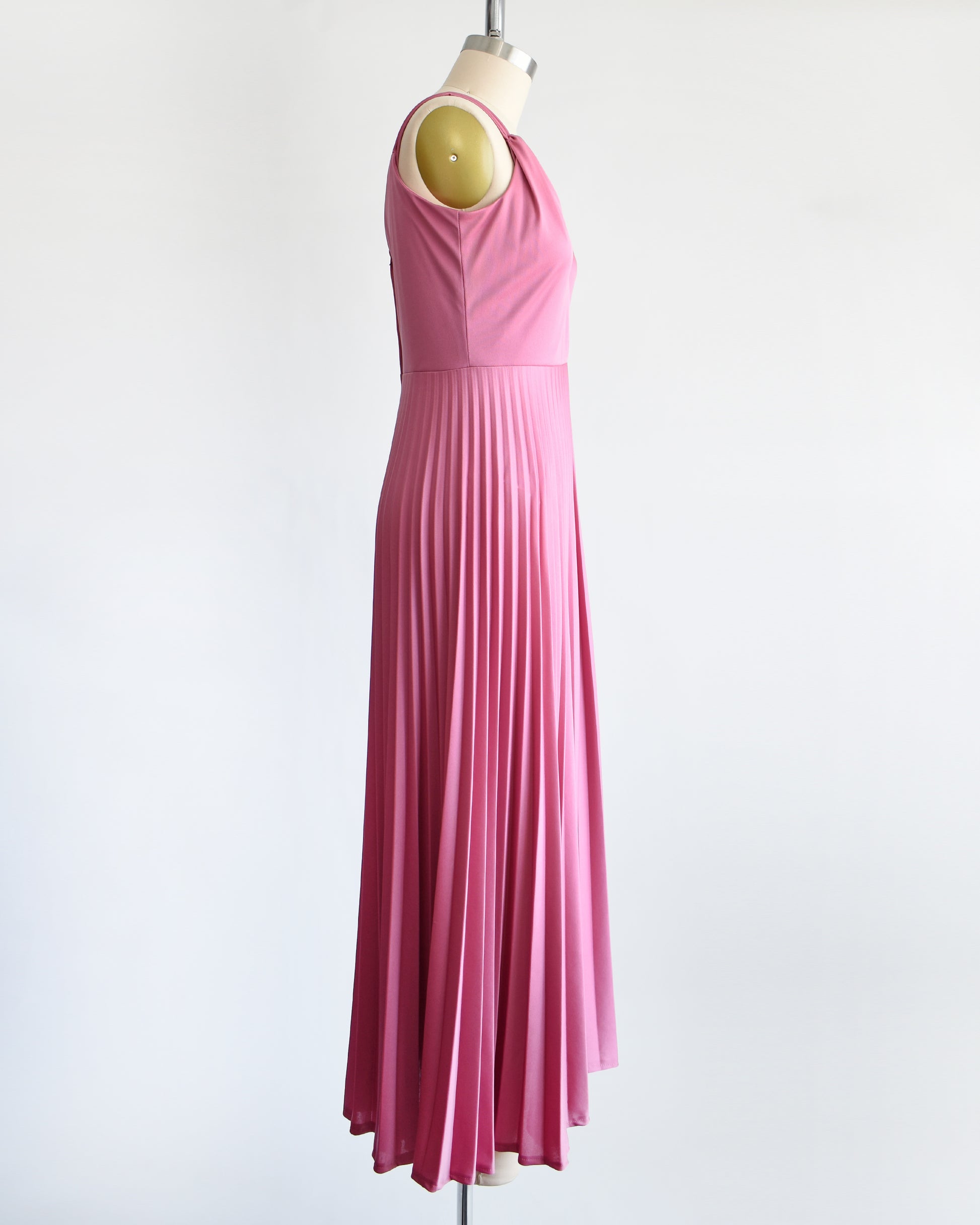 side view of a vintage 1970s dusty pink disco maxi dress that has a faux wrap front, and a long accordion pleated maxi skirt.