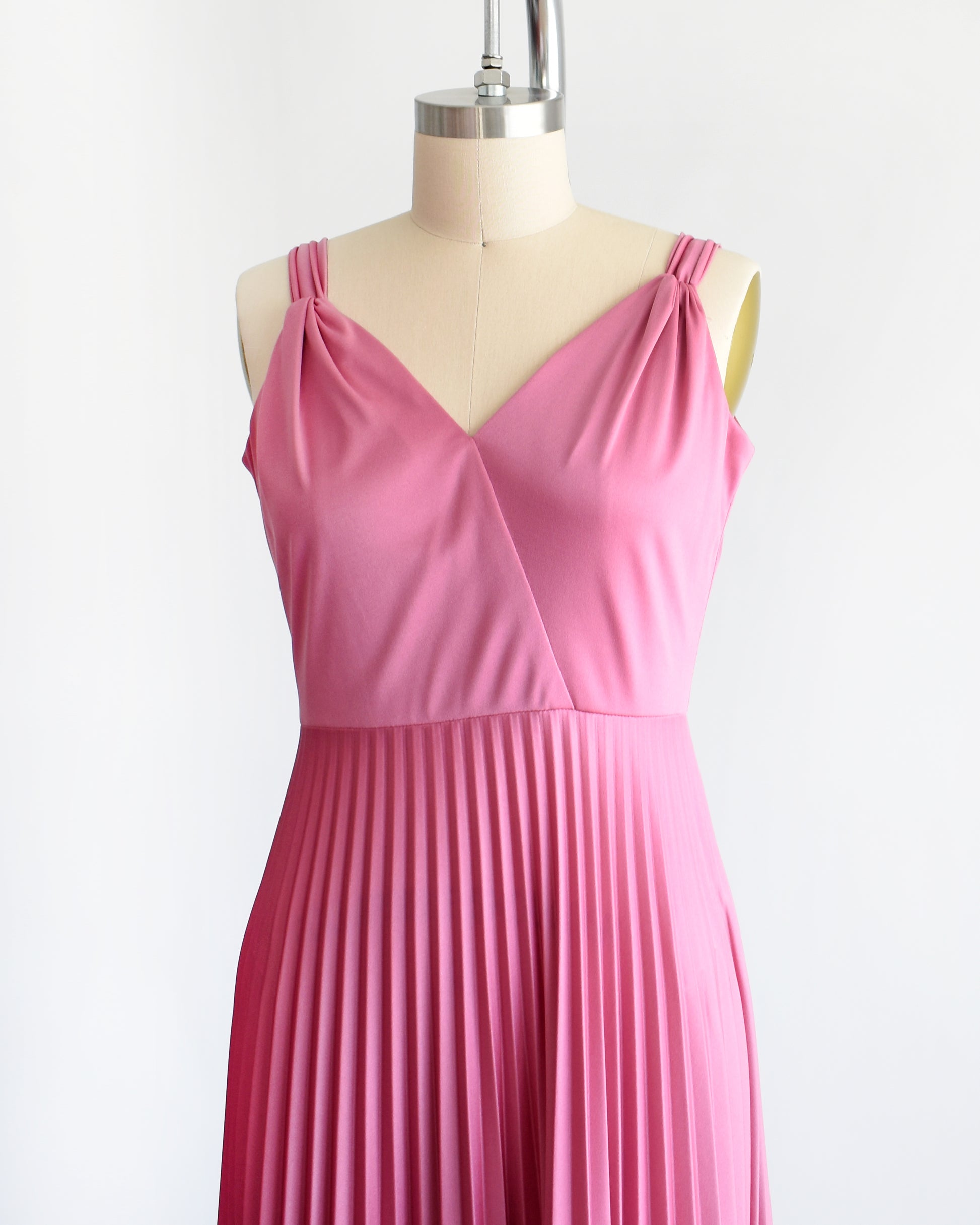 side front view of a vintage 1970s dusty pink disco maxi dress that has a faux wrap front, and a long accordion pleated maxi skirt.