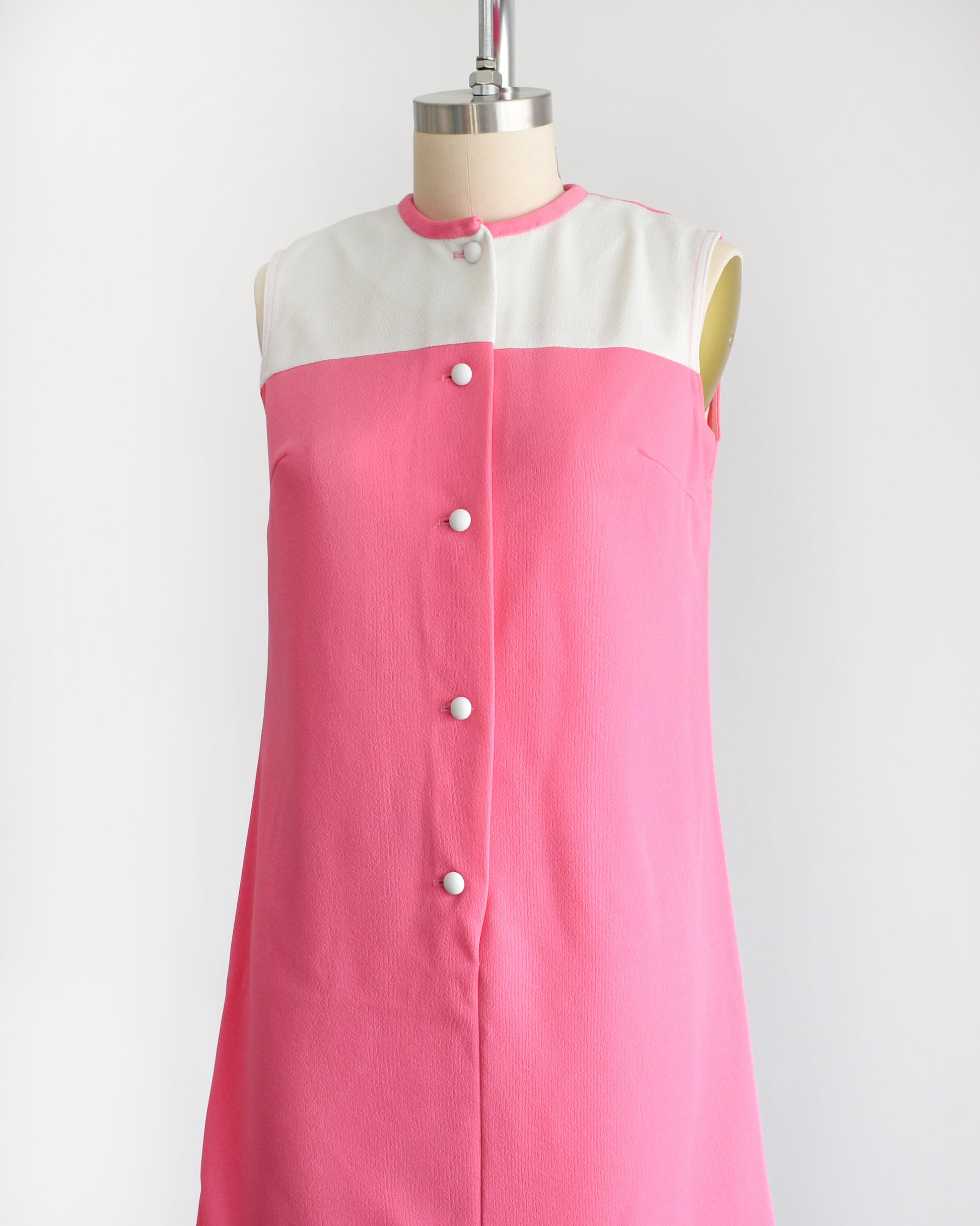 side front view of a vintage 1960s pink and white mod mini dress that has five white buttons down the front.